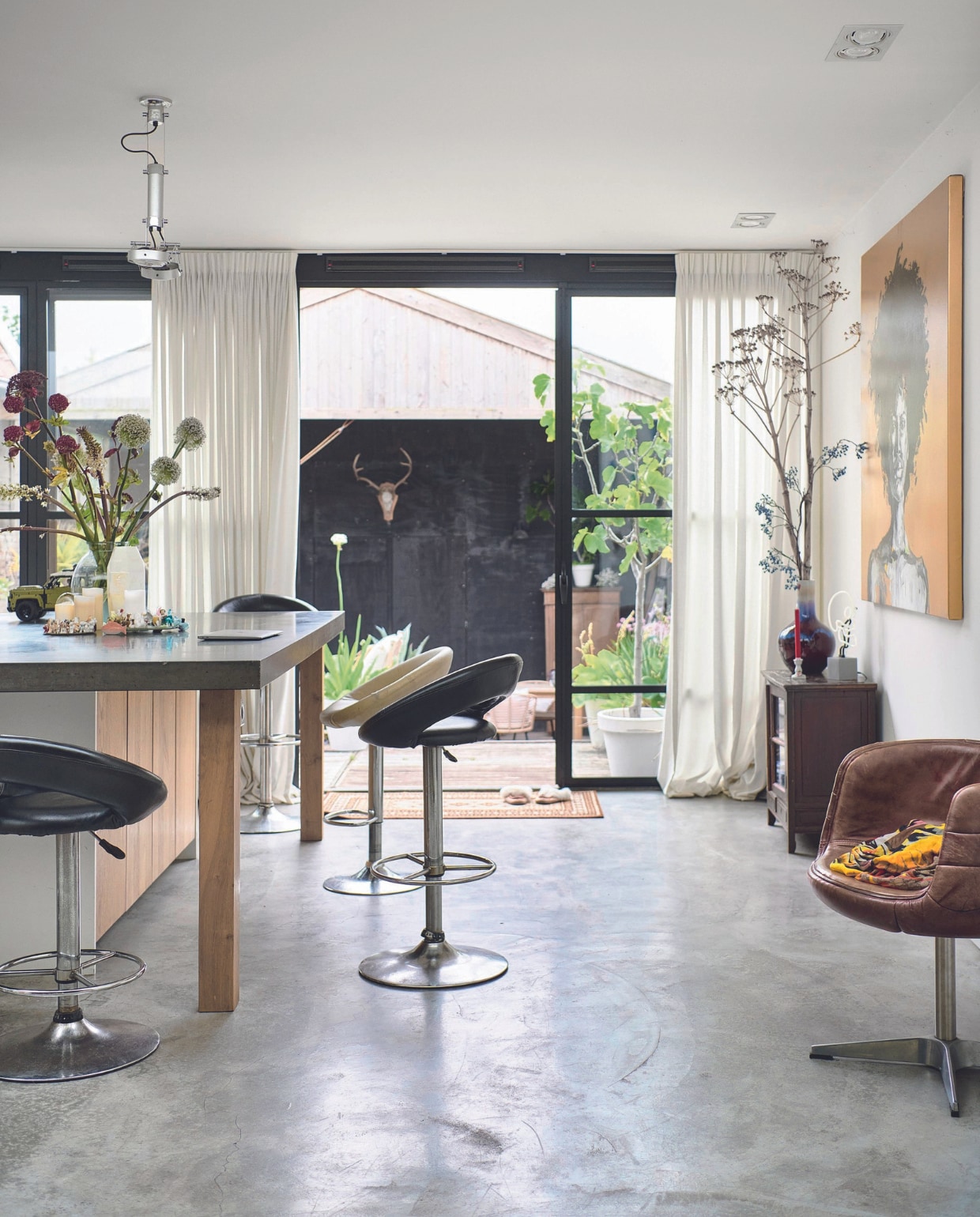 Keukenwerkblad met eettafel Koak Design, krukken uit een garagesale, kast uit Indonesië, kuipstoel Marktplaats, schilderij Aron Kroes. vtwonen 08-2024 | styling Marianne Luning | fotografie Sjoerd Eickmans