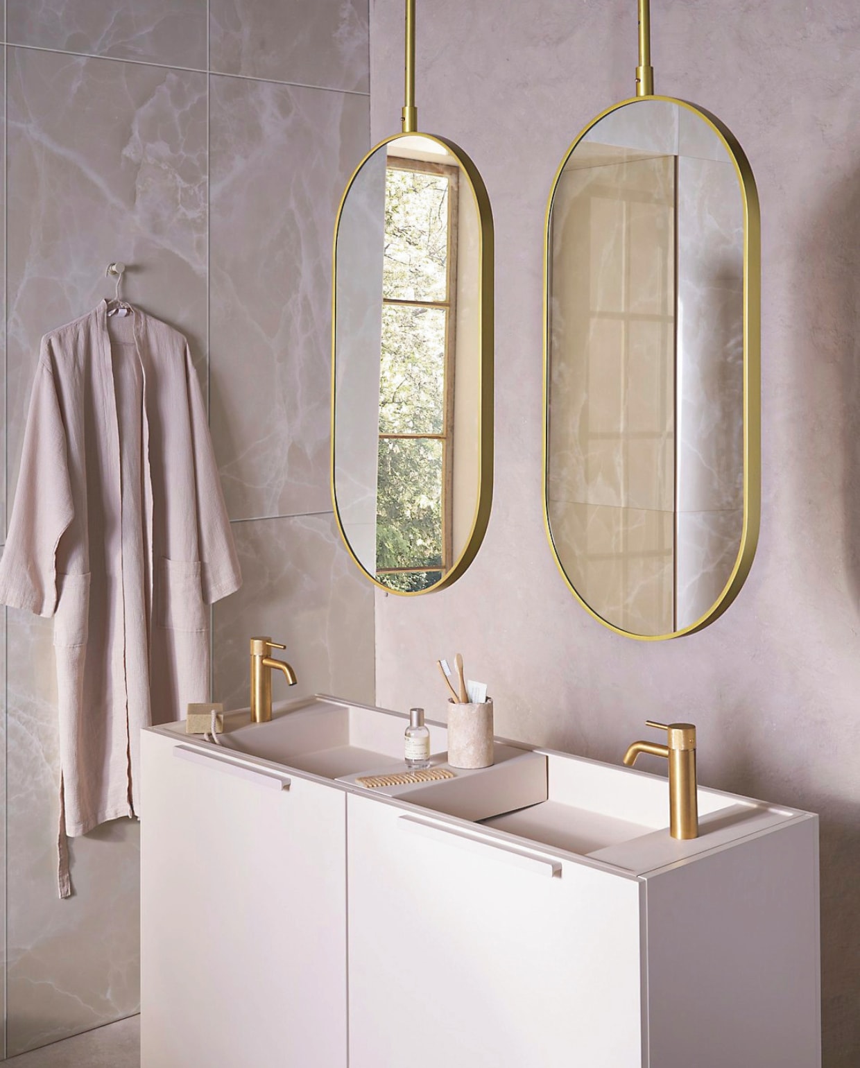 Op de wand tegels Onyx Crystal White, 60x120 cm, per m² € 92,50. Spiegels Oval in goud, 60x90 cm (bxh) € 550,-, ook verkrijgbaar in andere afmetingen. Top Solid onderkast in matzand, 124,6x44,4x90 cm (bxdxh) € 1300,-, Top Solid wastafel Wide in zand, 121x40,5x20 cm (bxdxh) € 1095,-, Top Solid plateau voor wastafel in zand, 36,8x15x8 cm (bxdxh) € 208,-. M.m.v. zarahome.com (beker, zeep, kimono),  plieger.nl (kranen Roma in geborsteld goud), lelabofragrances.com (parfum). vtwonen 09-2024 | styling Cleo Scheulderman | fotografie Jeroen van der Spek
