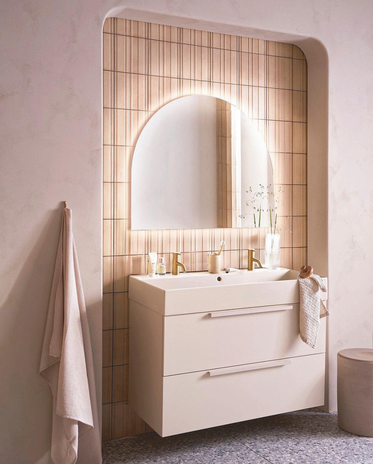 Op de wand tegels Earth Calce 3D Decor, 20x20 cm, per m² € 64,50. Op de vloer tegels Terrazzo Smoke Flakes, 60x120 cm, per m² € 74,50. Spiegel Design, half rond met indirecte verlichting, 100x80 cm € 998,-, ook verkrijgbaar zonder verlichting en in andere afmetingen. Kunststof onderkast Tidy in matzand, twee lades met handgreep, 120x40,5x40 cm (bxdxh) € 1362,-, Top Solid wastafel Wide in zand, twee kraangaten, 120x41x20 cm (bxdxh) € 1095,-. M.m.v. plieger.nl (kranen Roma in geborsteld goud), vtwonen.nl/shop (kruk van Serax), zarahome.com (badlaken, beker, zeep, kimono), lelabofragrances.com (parfum). Overig privébezit. vtwonen 09-2024 | styling Cleo Scheulderman | fotografie Jeroen van der Spek
