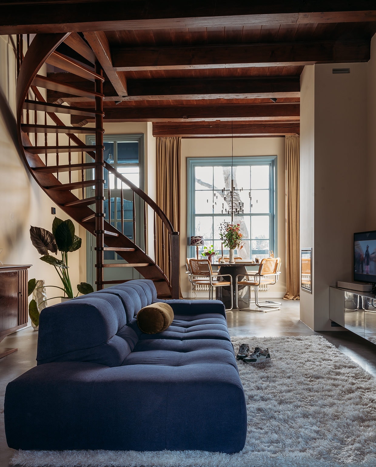 Muurverf White Tie van Farrow &amp; Ball. Lak kozijnen zijdeglans wit 6400 van Histor. Vloer Cem-Line Micro van Loos Betonvloeren. Bank Tufty Time van B&amp;B Italia via Marktplaats, laten stofferen door WeerMooi Meubels&amp;Stoffering. Fluwelen kussenrol Basiclabel. Vloerkleed Lea van Benuta. Art-decodressoir van Marktplaats, zelf opgeknapt. Lamp zelf samengesteld bij Madame Garage. Boekenstandaard teNeues. Bloempot Ruben van Karwei. Perzisch tapijt aan de wand van Hype pop-up, kunstwerk rechts zelfgemaakt. vtwonen 03-2021 | productie Coco Features | styling Laurien Deken | fotografie Inge Korver