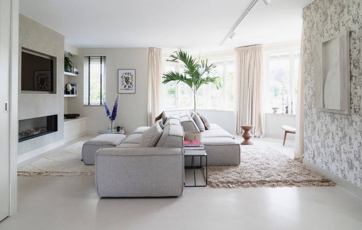 Vloer Microcement via TAV Microcement. Modulaire bank Edge van Fest Amsterdam. Bijzettafel Broste Copenhagen. Vaas op bijzettafel Zara Home. Televisie LG. Haard DRU. Poster aan de wand vintage. Kussens op bank o.a. NOX en via Loft. Plant Veitchia adonidia merrillii XL. Behang Dutch Walltextile. vtwonen 08-2021 | fotografie Muk van Lil