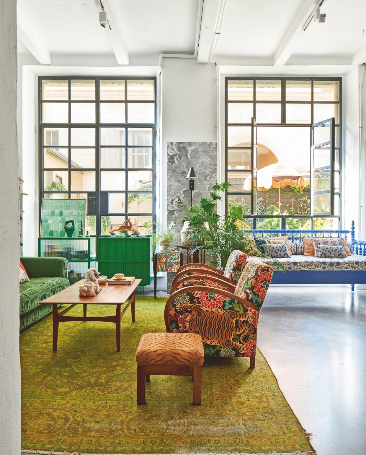Perzisch tapijt, salontafel, poef, plantentafels vintage. Vintage stoelen bekleed met stof van Gastón y Daniela. Daybed, kleine kussens op het daybed, het beklede daybedmatras en accessoires op groene kasten Nap Atelier. Bank, groen dressoir, dressoir met geribbeld glas, effen en gestreepte kussens op het daybed en groen accessoire HKliving. Wandlamp House Doctor.