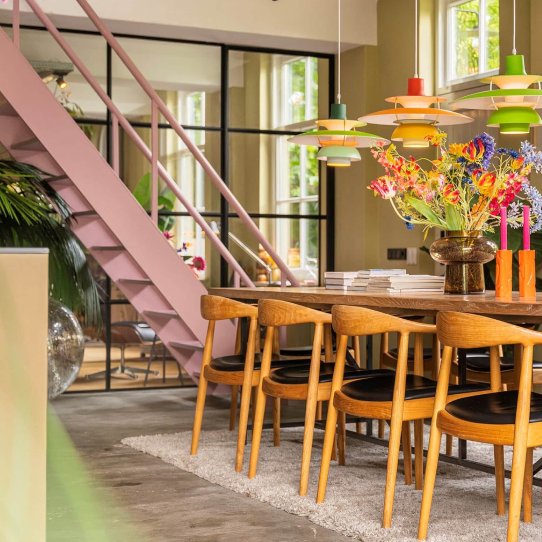 Kleurrijke eetkamer met houten stoelen, bloemen en een roze trap