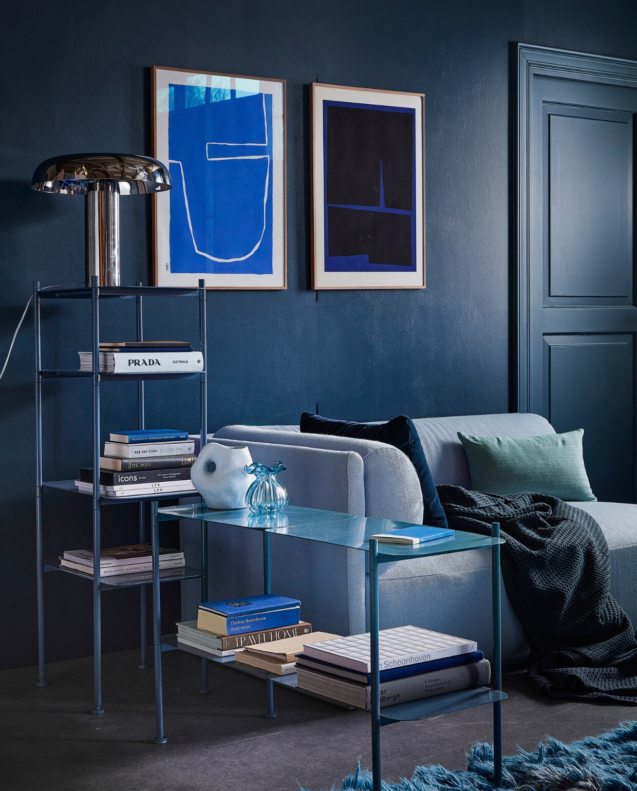 Muurverf en houtverf Steel Blue. Bank Bolster longchair in kleur Vidar 723 Boekenkasten River in Ocean Blue en Tafellamp Mushroom, vloerkleed Rough Waters, Plaid van Vandyck, donkerblauw kussen van Hay. Organische vaas van Madam Stoltz, glazen vaas Kataja van Nordal zijden kussen van Urban Nature Culture, 50x30 cm . Boek van Prada . Art print links The Route van Leise Dich Abrahamsen,art print rechts Blue Geometric 02 van Bycdesign Studio, Overig privébezit. vtwonen 01-2023 | styling Marlies Does | fotografie Peggy Janssen | decor Studio Milo