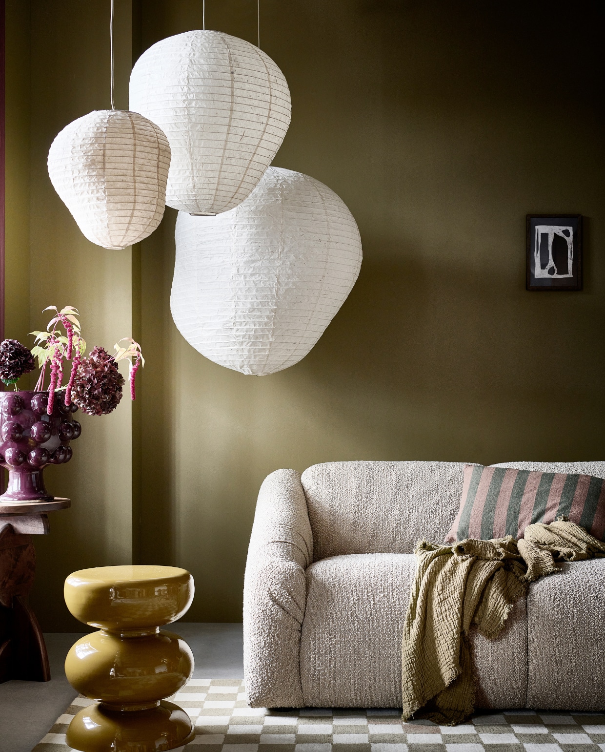 Rijstpapieren hanglampen Kurbis, 38x40 cm, 57x60 cm en 75,5x80 cm (Øxh), vanaf € 79,- (fermliving.com). 4-zitsbank Cooper, 300x97x72 cm (bxhxd) € 2195,-, metalen bijzettafel Mala 36x46 cm (Øxh) € 125,-  (loods5.nl). Vloerkleed Check, wol en katoen, 170x240 cm € 299,-, kussen Linen Stripe van By Fonq, katoen en linnen € 34,99, wollen plaid Mono van Hay in Olive, 180x130 cm € 115,- (vtwonen.nl/shop). Mangohouten bijzettafel Nori van Woood, 40x60 cm (Øxh) € 129,- (basiclabel.nl). Poster Composition No2 van Lone Fox, 21x30 cm € 10,95, houten fotolijst 21x30 cm € 10,95 (desenio.nl). Paarse keramieken pot € 84,99 (karwei.nl). Muurverf Scented Cumin No. 34 van Lab Paint, 1 liter € 51,- (vestingh.nl). vtwonen 01-2024 | styling Kim van Rossenberg | fotografie Sjoerd Eickmans