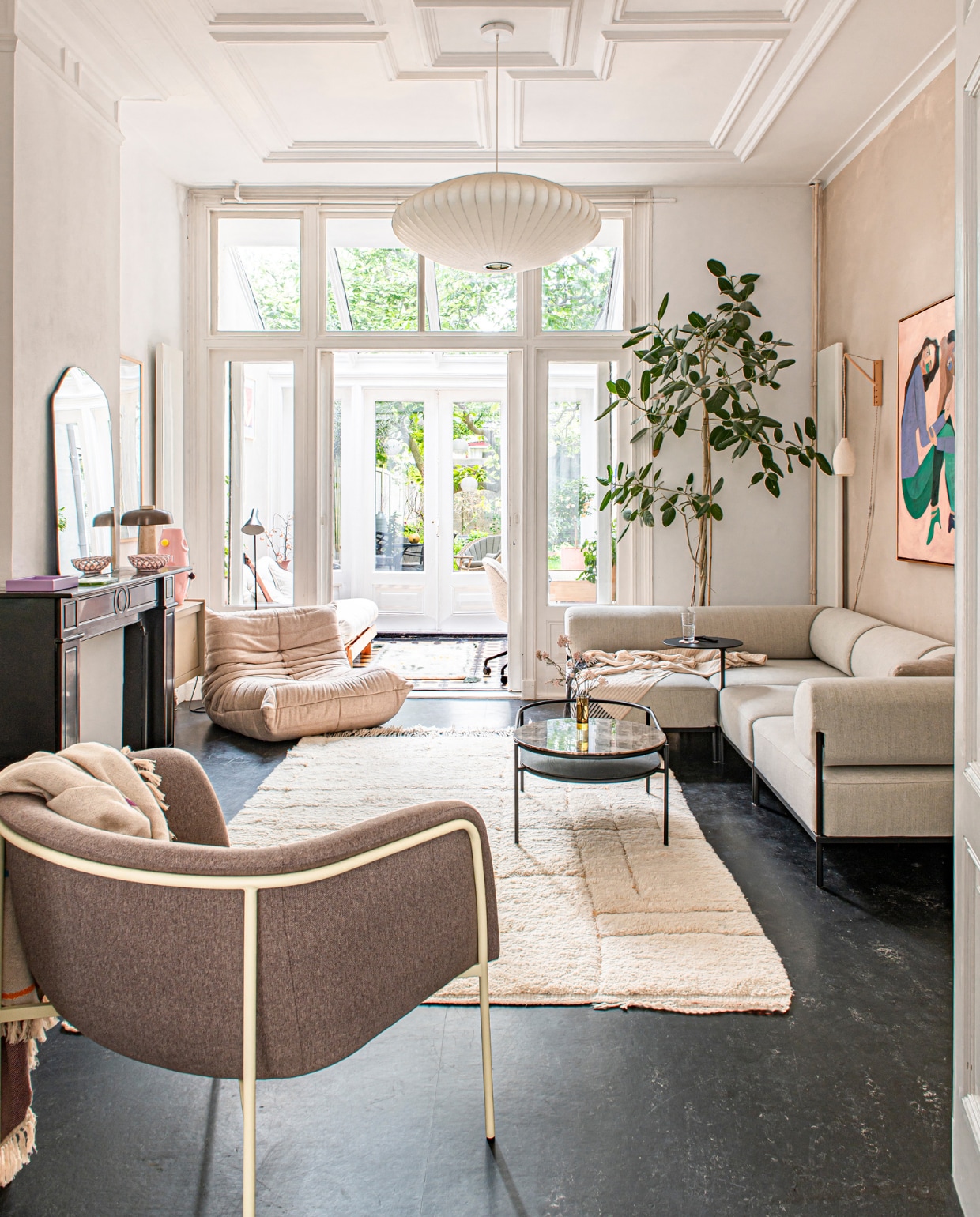 Lamp Saucer Bubble van George Nelson, schilderij van Anne Mei Poppe, bank Noah Living, koffietafel Woud, fauteuil Togo van Ligne Roset, roze vaas Malwina Konopacka, vloerlamp Arne Jacobsen voor Louis Poulsen, alle muurverf Kalkliter. Lamp, schaal en spiegel op schoorsteen vintage. Spiegel en vloerkleed HKliving. Stoel voorgrond Hübsch. Overig onbekend.