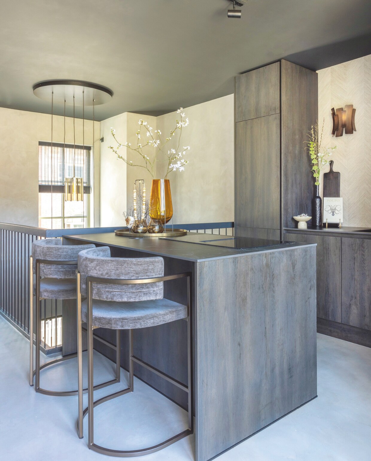 De keuken met keukenkastjes van Sherwood burned wood is gerealiseerd door Huysinc. Het werkblad van keramiek is van Jetstone en de kraan van Quooker. De hoge stoelen en de wandlampen zijn van Rapture Interior Luxury. Op de muur is gekozen voor behang van Arte. stijlvol wonen 09-2024 | fotografie Anneke Gambon