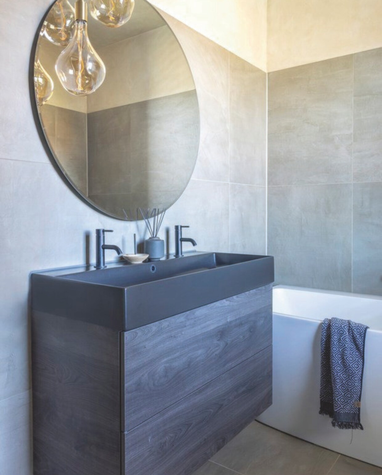 Het wastafelmeubel is van Detremmerie, de messing hanglamp erboven is van Tala, de spiegel van Spiegelpracht. De vloer en de wand zijn betegeld met tegels Concrete in kleur Smoke van Piet Boon by Douglas &amp; Jones. stijlvol wonen 09-2024 | fotografie Anneke Gambon