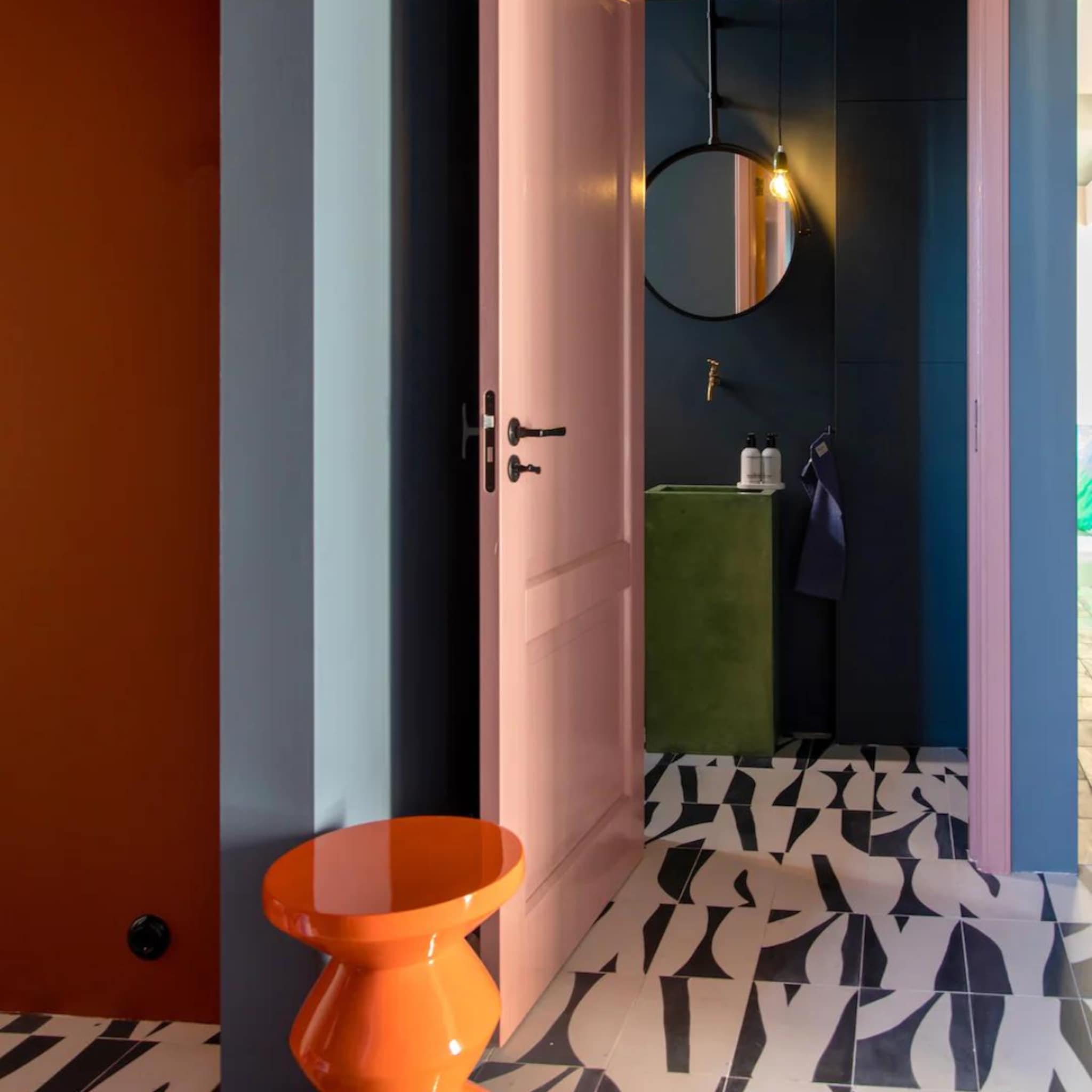 Kleurrijke hal met een grafische vloer, roze deur en oranje bijzettafel