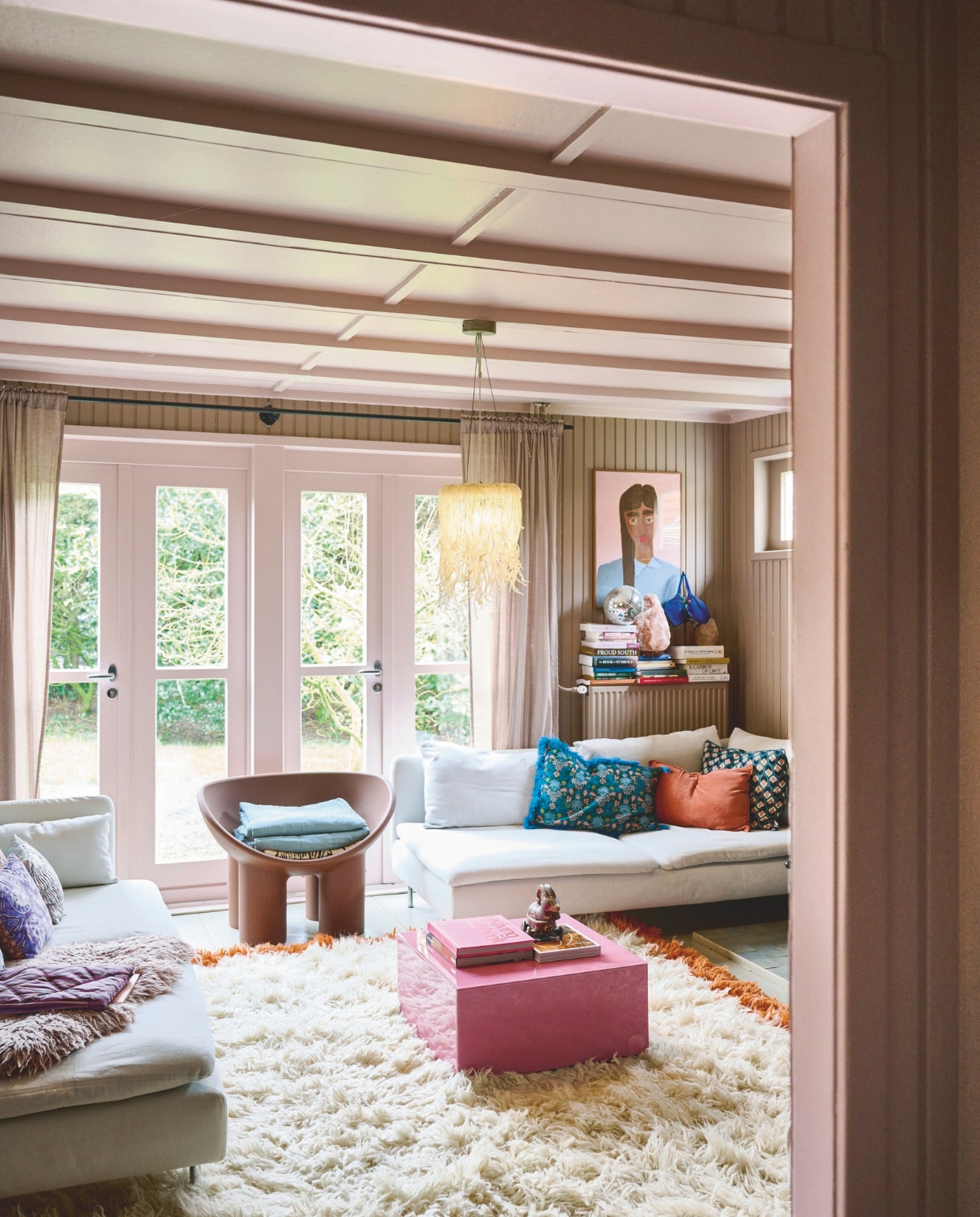 > Muurkleur Dead Salmon, oude pakhuisvloer Shaded White, plafond- en kozijnenkleur Calamine van Farrow & Ball. Gordijnen, bank en fluffy kleedje Ikea. Vloerkleed, salontafel, boeken erop, kussen HKliving, hanglamp Madam Stoltz, plaid Jysk. Kussens links Doris HKliving, kussens rechts Sissy-Boy, fauteuil Driade, wandkleed op stoel Anna + Nina, schilderij eigen werk. Op de boeken: discobal Xenos, zoutsteen Eco Plaza, tas  vtwonen 10-2024 | styling liza wassenaar | fotografie sjoerd eickmans