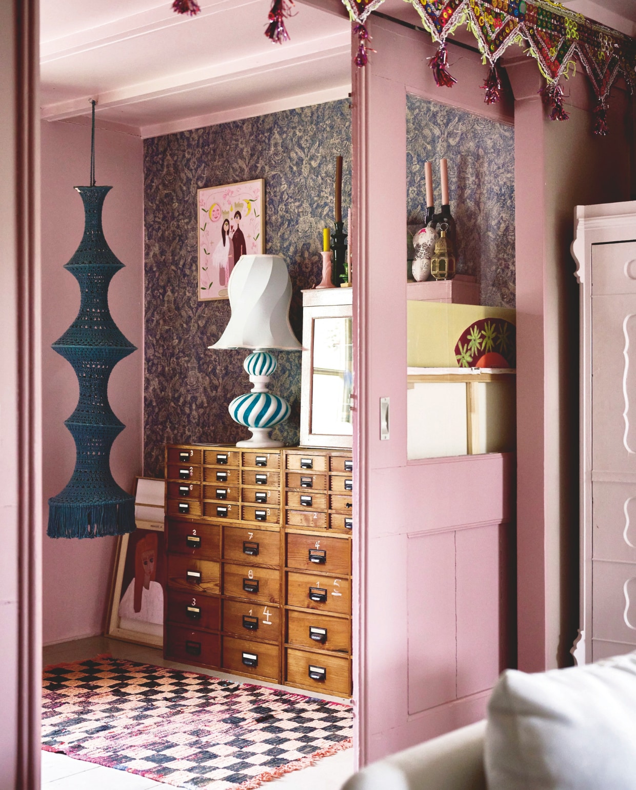 Behang Arte Travellers, vintage vitrinekast in Sulking Room Pink van Farrow &amp; Ball, hanglamp Elpelut, tafellamp HKliving, archiefkast Marktplaats, witte kast antiekwinkel, slinger La Galeria Elefante. vtwonen 10-2024 | styling liza wassenaar | fotografie sjoerd eickmans