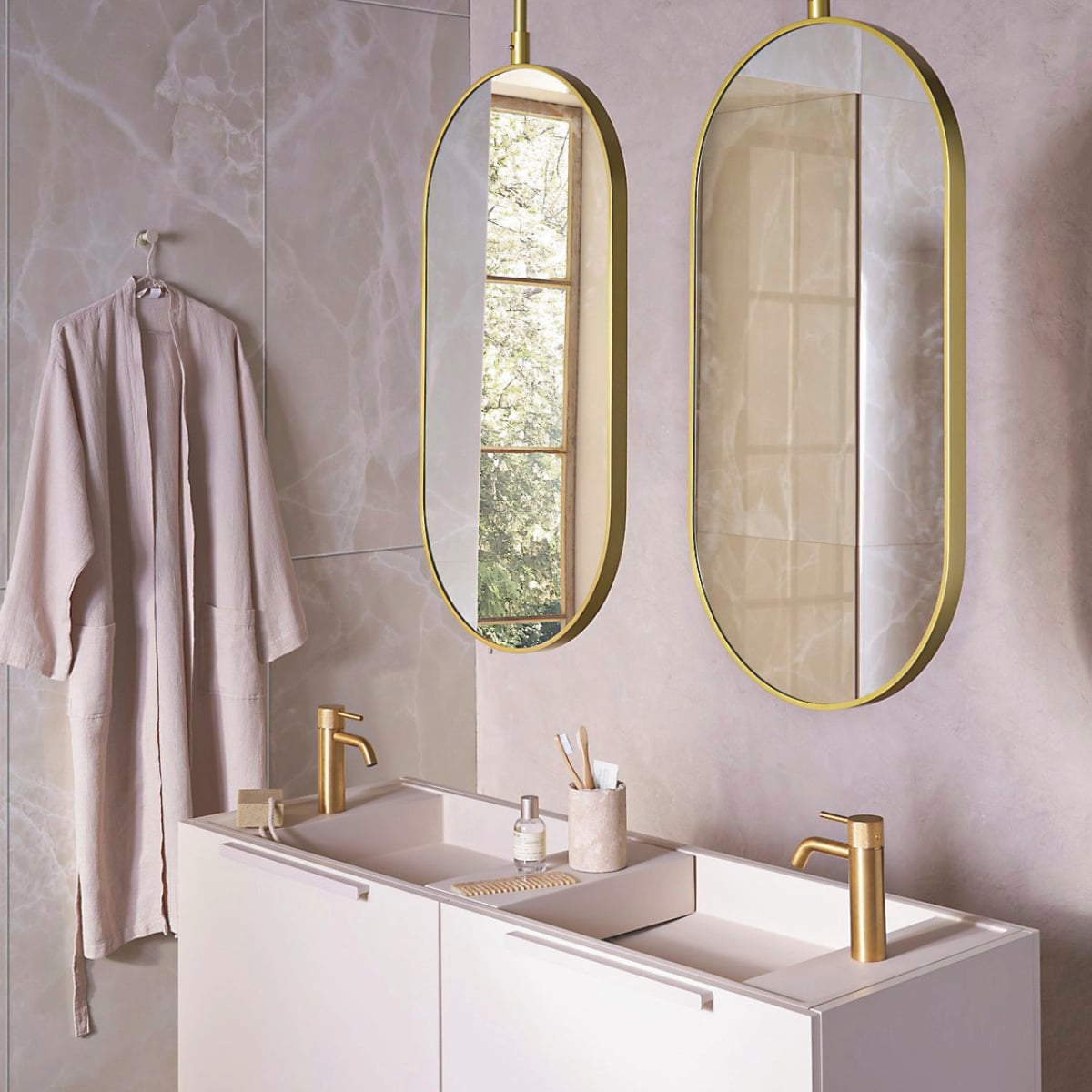 Op de wand tegels Onyx Crystal White, 60x120 cm, per m² € 92,50. Spiegels Oval in goud, 60x90 cm (bxh) € 550,-, ook verkrijgbaar in andere afmetingen. Top Solid onderkast in matzand, 124,6x44,4x90 cm (bxdxh) € 1300,-, Top Solid wastafel Wide in zand, 121x40,5x20 cm (bxdxh) € 1095,-, Top Solid plateau voor wastafel in zand, 36,8x15x8 cm (bxdxh) € 208,-. M.m.v. zarahome.com (beker, zeep, kimono),  plieger.nl (kranen Roma in geborsteld goud), lelabofragrances.com (parfum). vtwonen 09-2024 | styling Cleo Scheulderman | fotografie Jeroen van der Spek