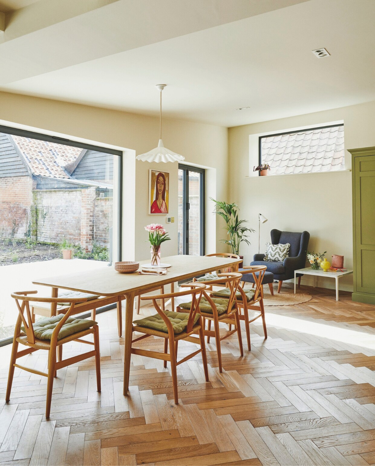 Stoelen Wishbone Carl Hansen &amp; Sons, stoelkussens H&amp;M Home, eettafel Heals, roze vaas Vanil, schilderij Rusty Studio, muurverf Clunch van Farrow &amp; Ball. Vloer eikenhouten parket. vtwonen 11-2024 | styling Kay Prestney | fotografie Brent Darby