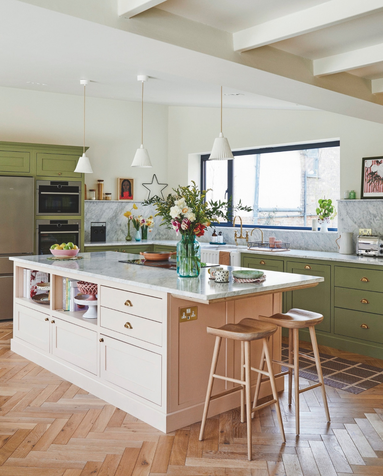 Op maat gemaakte keuken geverfd in Olive en Potted Shrimp van Farrow & Ball, messing handgrepen en kranen Devol,krukken Neptune, ovens en koelkast Aeg, schilderij Rusty Studio, loper Pappelina, roze fruitschaal Vanil, muurverf Clunch van Farrow & Ball. vtwonen 11-2024 | styling Kay Prestney | fotografie Brent Darby