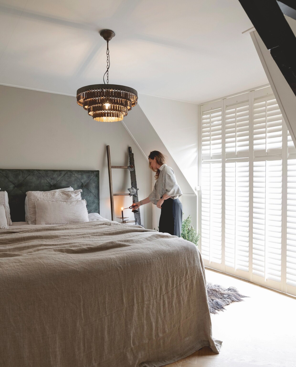 Met de kamerhoge shutters is de lichtinval makkelijk te regelen. Op de vloer ligt eiken visgraatparket, de hanglamp en de kaarsenhouder zijn van Hoffz. De XL-bedsprei komt van Zara Home. vtwonen landelijk 07-2024 | fotografie Jonah Samyn