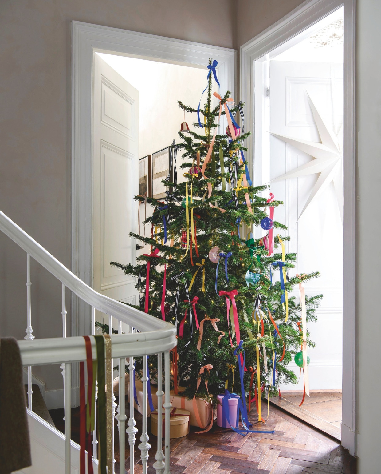 Natuurlijke kerstboom Nordmann, 240 cm (h) € 55,- (buitengoeddeboomgaard.nl). Roze-rode en blauw-groene glazen strikken € 14,95 (klevering.com). Effen glazen ballen in blauw, groen, roze en lila van House of Seasons, set van 4 € xxxx (vtwonen.nl/shop). Satijnen lint, vanaf van 8 meter per rol € 3,29 (pipoos.nl). Overig privébezit. vtwonen 12-2024 | styling Marit Saladini | fotografie Louis Lemaire