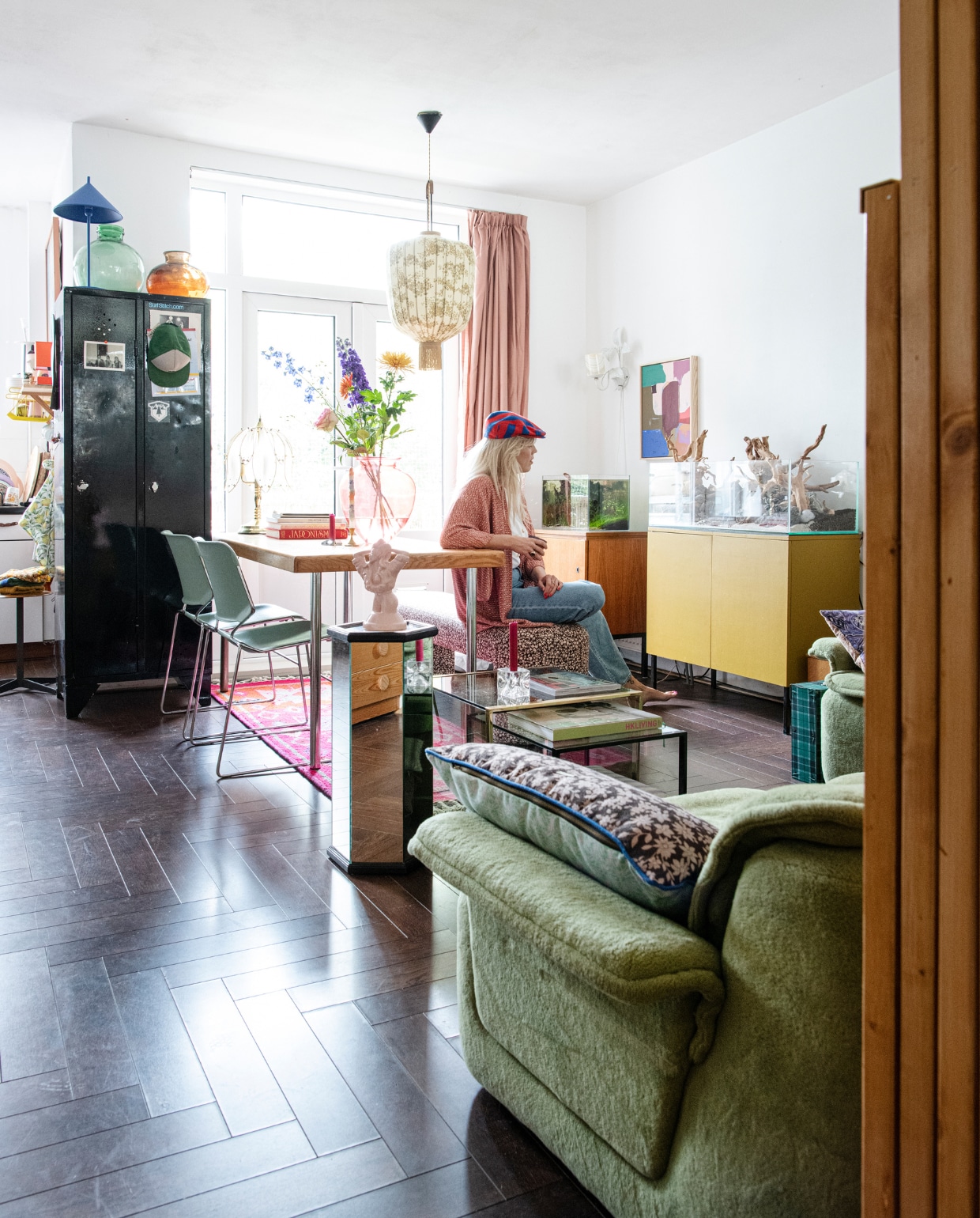 Groene fluwelen bank @vanvintagetayko. Kussens, roze tapijt en bankje Doris voor HKliving. Eettafel Marktplaats. Stoelen Krueger Matrix. Roze vaas Rataplan. Alle kandelaars cadeau gekregen. Vierkante koffietafel Noppes, zeshoekige koffietafel De zaak van Sjaak. Roze beeld en lamp aan de muur Fortune Flea. Zwarte kast gekregen. Groene vaas Van Dijk &amp; Ko, vazen op de kast Vok Jong Bloemen en Planten. Hanglamp Vintage Depot. Gordijnen Noordermarkt. Schilderij HKliving. Lage kast tegen de muur links gevonden langs de weg met klein aquarium van Rainer. Kast rechts met terrarium gemaakt door Mark en z’n opa. Vloer zat al in het huis. vtwonen 02-2022 | productie Insidehomepage | styling Kim Timmerman | fotografie Louis Lemaire