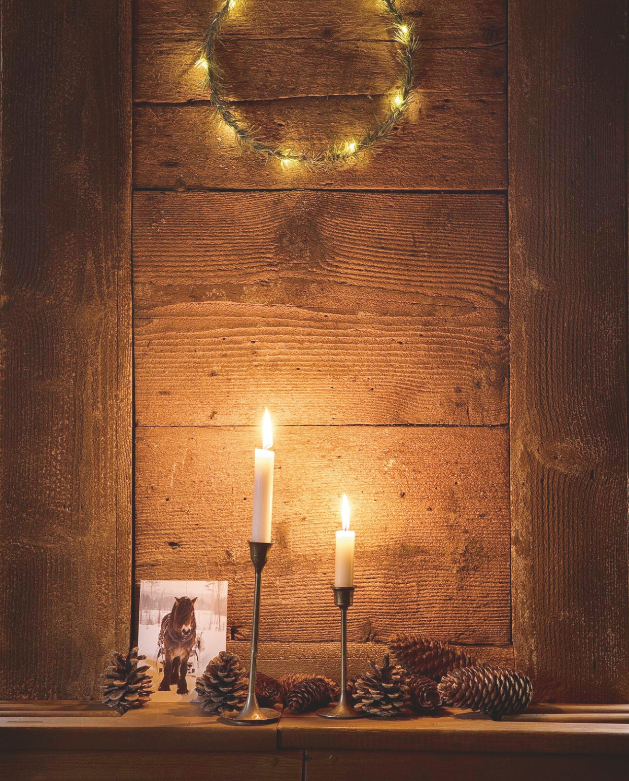 Het oude hout op de muren en plafonds heeft een patine, dat de de sfeer uniek maakt. De natuurlijke decoraties met dennenappels en -takken en lichtjes versterken het kerstgevoel. vtwonen landelijk 07-2024 | styling Miriam Hannemann | fotografie André Reuter