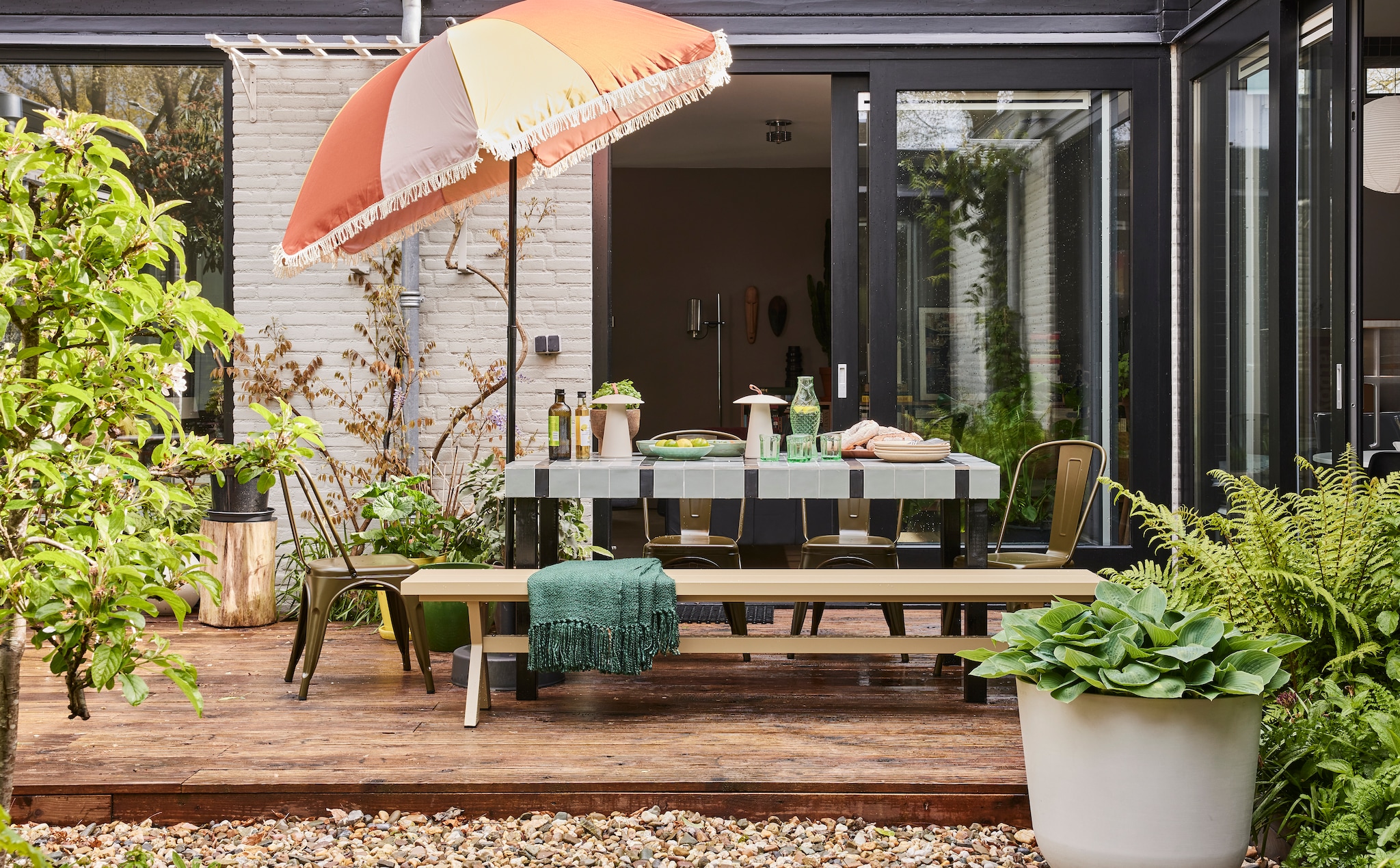 Tafel op maat gemaakt vanaf € 175,- (com-anders.nl), betegeld met vtwonen wandtegel Chop in Salvia, 10x10 cm € 79,90 per m² en wandtegel Chop Nero, 5x15 cm € 79,90 per m² (douglasjones.nl). Parasol € 49,99 (karwei.nl). Aluminium bank Delta van Exotan, 220x35x45 cm (lxbxh) € 299,-, plaid van Malagoon in Forest Green, 125x150 cm € 49,99, witgrijze plantenpot van Ecopots, 55 cm (Ø) € 99,- (vtwonen.nl/shop). Op tafel: draadloze lamp Ara van Nordlux € 129,95, viskaraf en glazen van Paola Navone voor Serax € 95,50, zeegroene saladeschaal, € 33,50 en dinerborden by fonq € 49,99 per 4 (shop. vtwonen.nl). Eetkamerstoel Afternoon van vtwonen € 79,95 (basiclabel.nl). Overig privébezit. vtwonen tuinspecial 01-2025 | styling Fietje Bruijn | fotografie Alexander van Berge