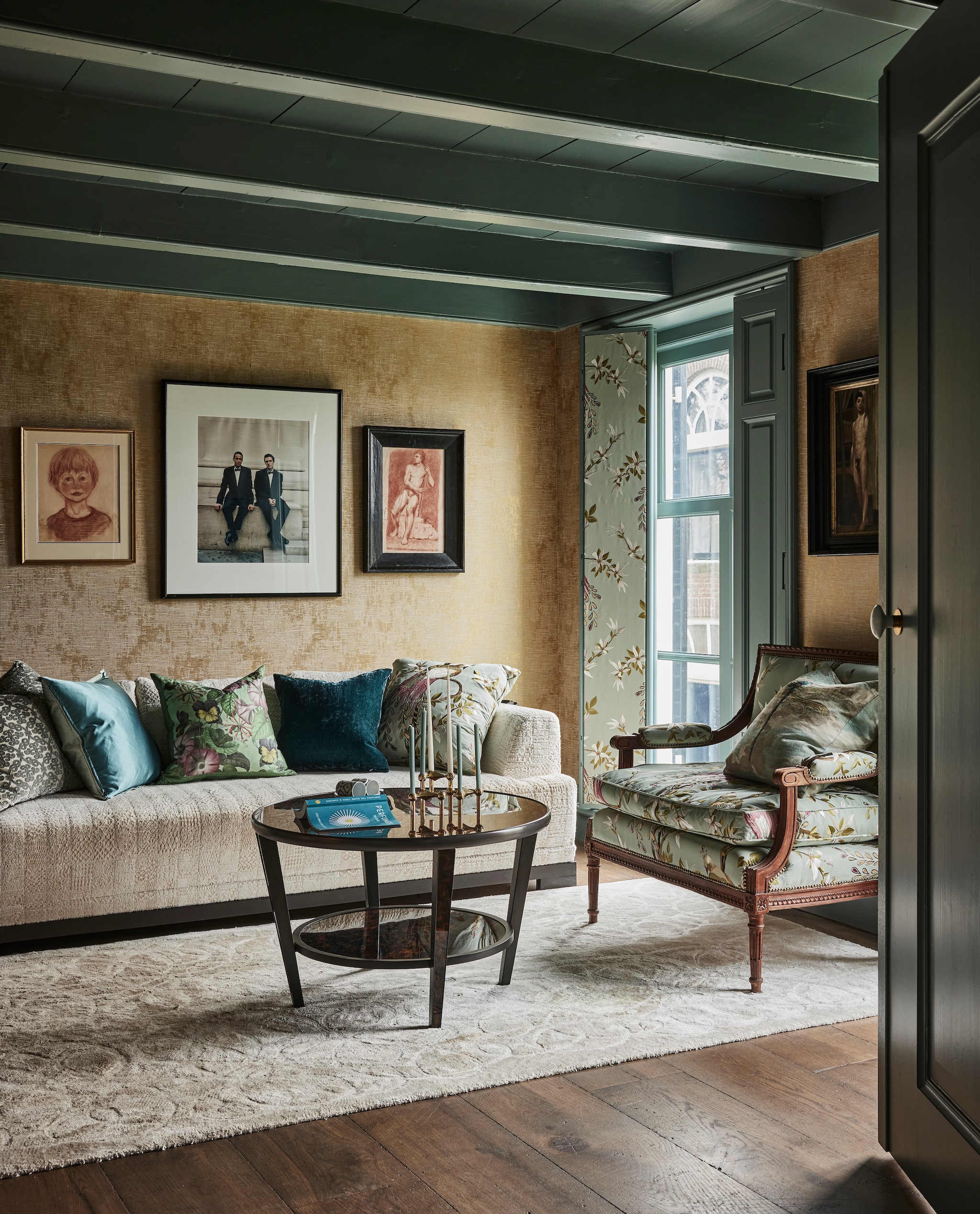 Luiken en fauteuil bekleed met stof Paradiso van Nina Campbell via Osborne & Little. Salontafel Arno Tortoiseshell van William Yeoward. Vloerkleed en kussens Designers Guild via Wilhelmine van Aerssen Agenturen. Bank Canapé California in stof Baalbec Nobilis. Kaarsenstandaard Stoff Nagel. Houten vloerdelen van Landgoed Twickel. Kunst v.l.n.r. schets van Joris als kind, foto onbekend, studieschets. Kleur houtwerk Kerkgrijs Midden van Vettewinkel. vtwonen landelijk 01-2025 | styling Marianne Luning | fotografie Alexander van Berg