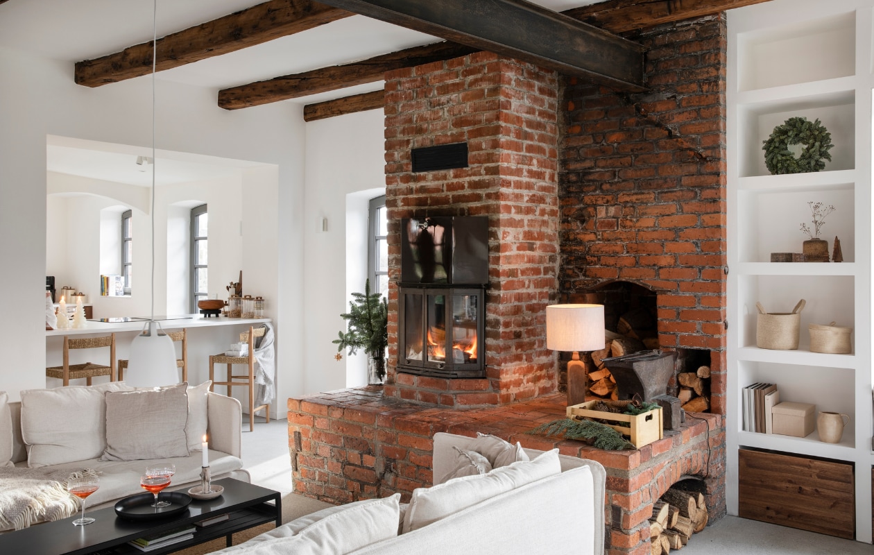 Originele haard. Witte hanglamp Clover van Eva Solo. Houten barkrukken met rieten zittingen Zara Home. Open inbouwkast zelfgemaakt. vtwonen 12-2024 | styling miriam hannemann | fotografie andré reuter