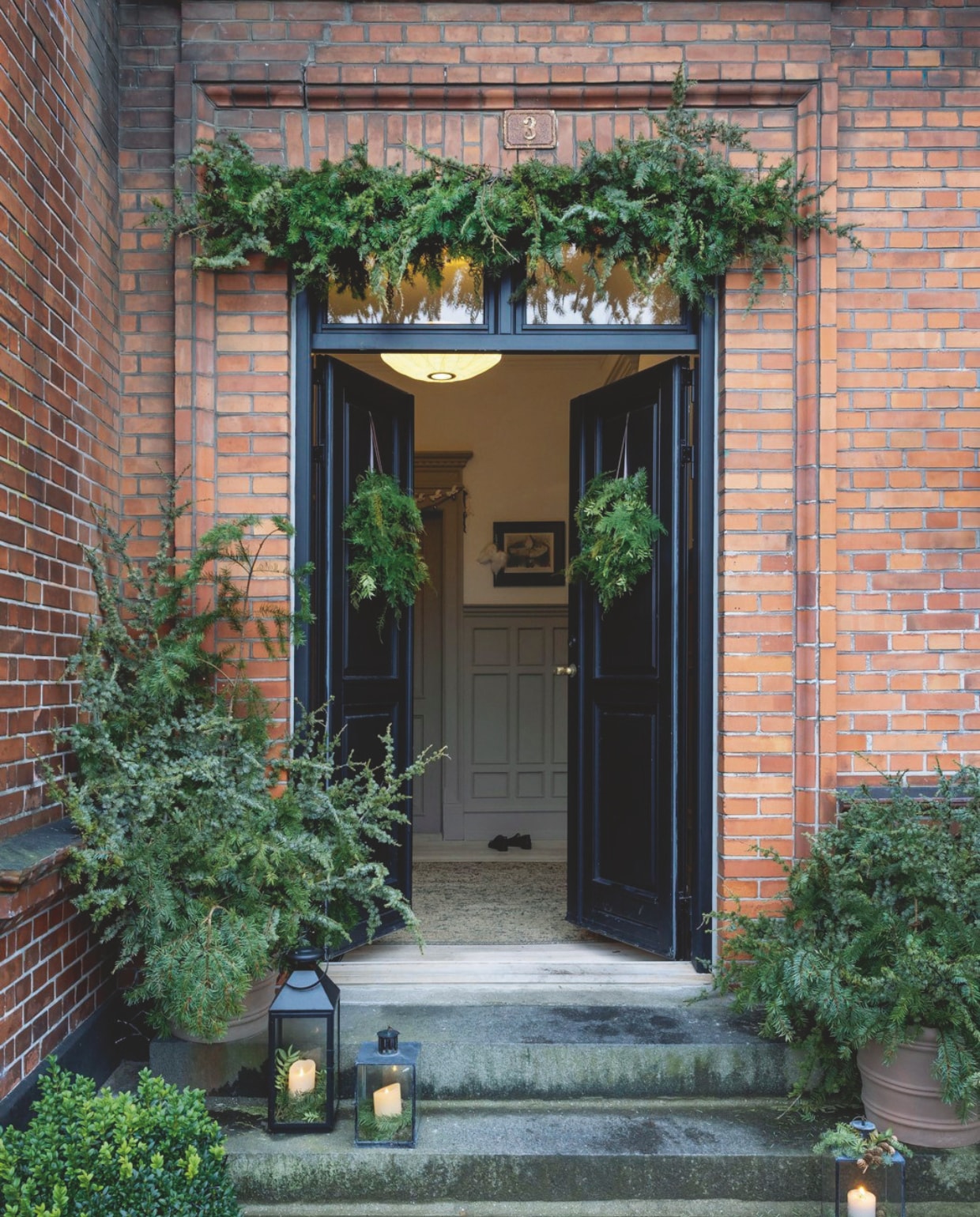 Met een guirlande boven de voordeur en kransen ertegen krijgt het huis in een handomdraai een kerstsfeer.  vtwonen 12-2024 | styling Rikke Graff Juel | fotografie Christina Kayser Onsgaard