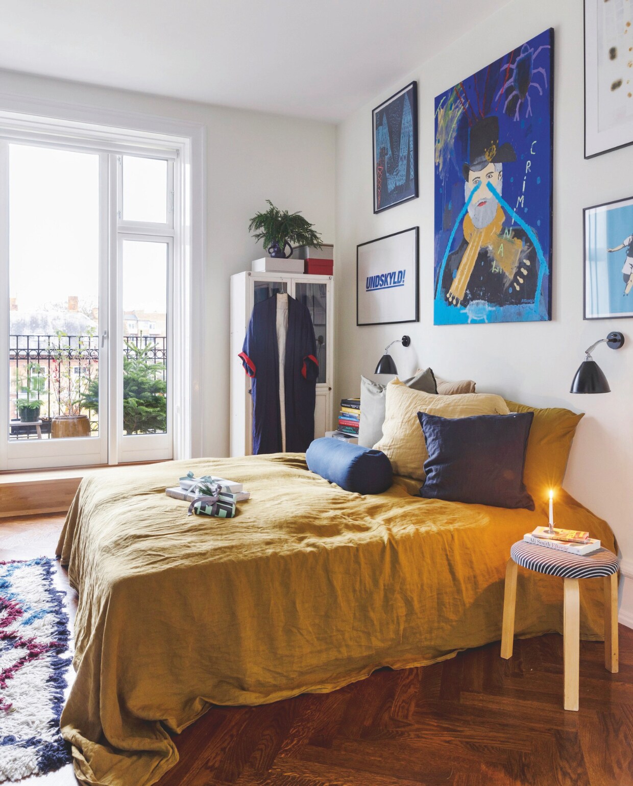 Een mix van blauwe prenten en schilderijen van Tal R, Frederik Ibfelt, Nicholas Koshkosh, Jan Oksbøll Callesen en Banksy. Beddengoed Merci, kruk van Alvar Aalto van Artek, bekleed met stof van Nørgaard, bedlamp Bestlite van Gubi. vtwonen 12-2024 | styling Rikke Graff Juel | fotografie Christina Kayser