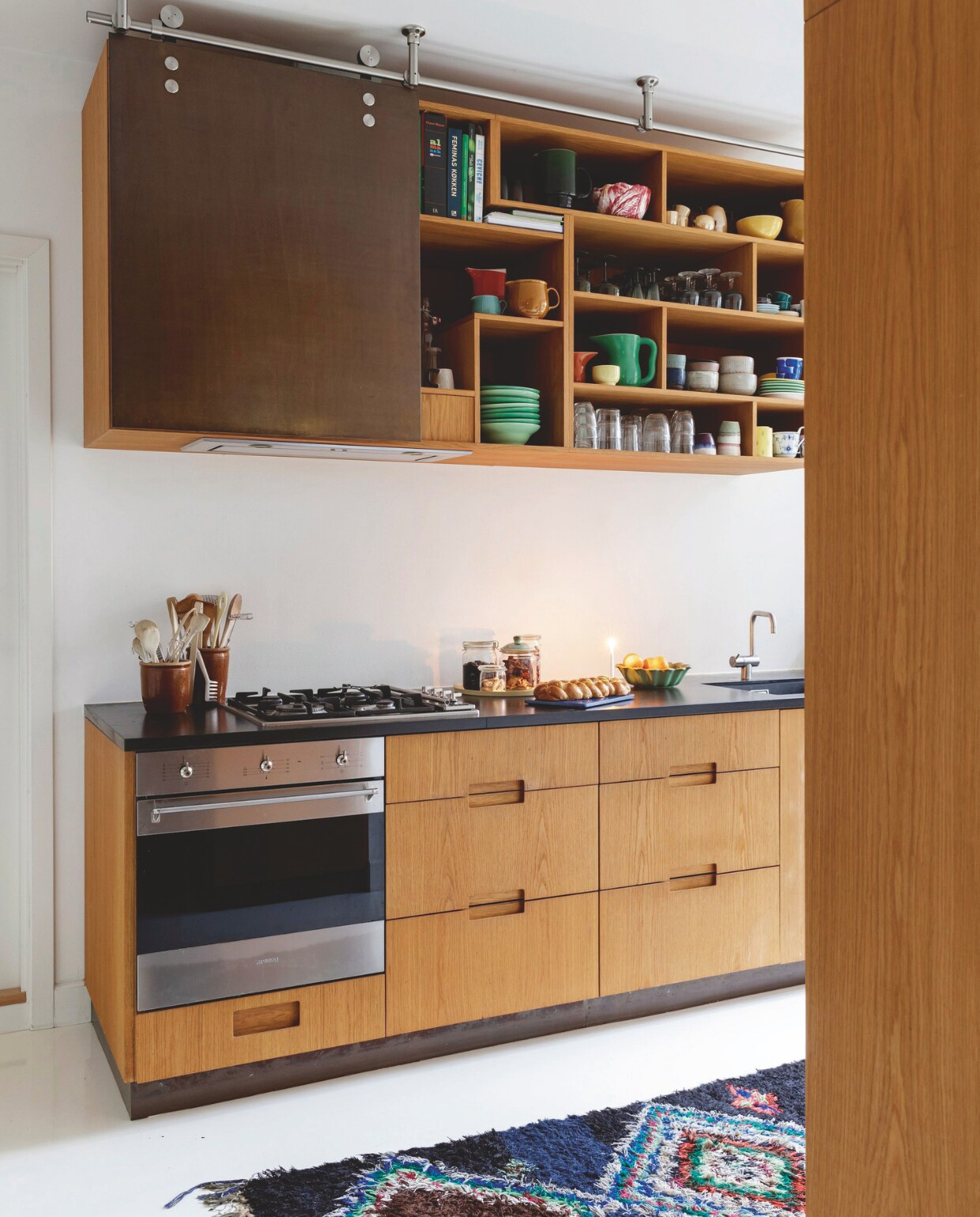 De eikenhouten keuken met werkblad van zwart natuursteen is maatwerk van Studio Flemming Lindholdt. Serviesgoed een mix van de Ursula serie van Royal Copenhagen, schalen van pottenbakker Mette Seedorff, vakantiesouvenirs en erfstukken. vtwonen 12-2024 | styling Rikke Graff Juel | fotografie Christina Kayser