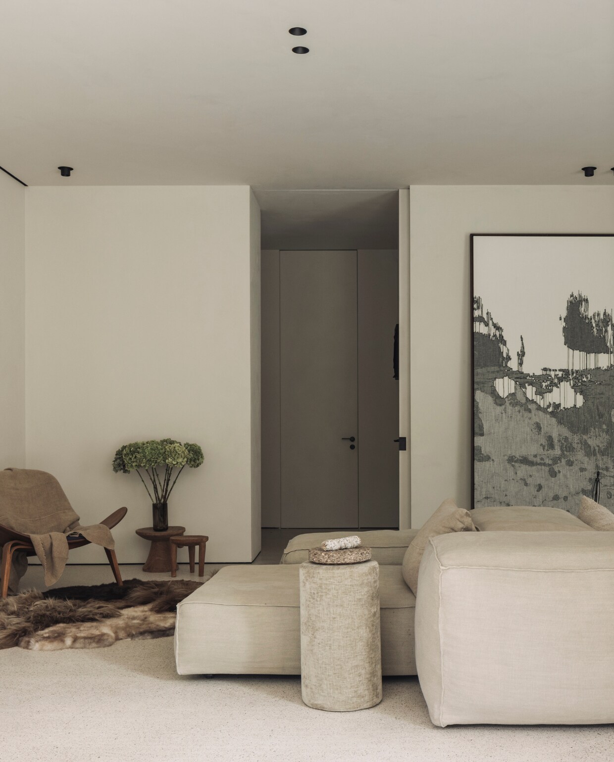 In de hoek de Shell Chair van  van Carl Hansen ontworpen door Hans J. Wegner, erop een plaid van Isabelle Yamamoto. Bijzettafeltjes van een vlooienmarkt in Marrakesh. Vacht op de vloer van Carine Boxy. Loungebank en poef Extrasoft van Living Divani met kussens van Isabelle Yamamoto. Kunstwerk rechts Nathalie Van der Massen. stijlvol wonen 01-2025 | fotografie Tijs Vervecken