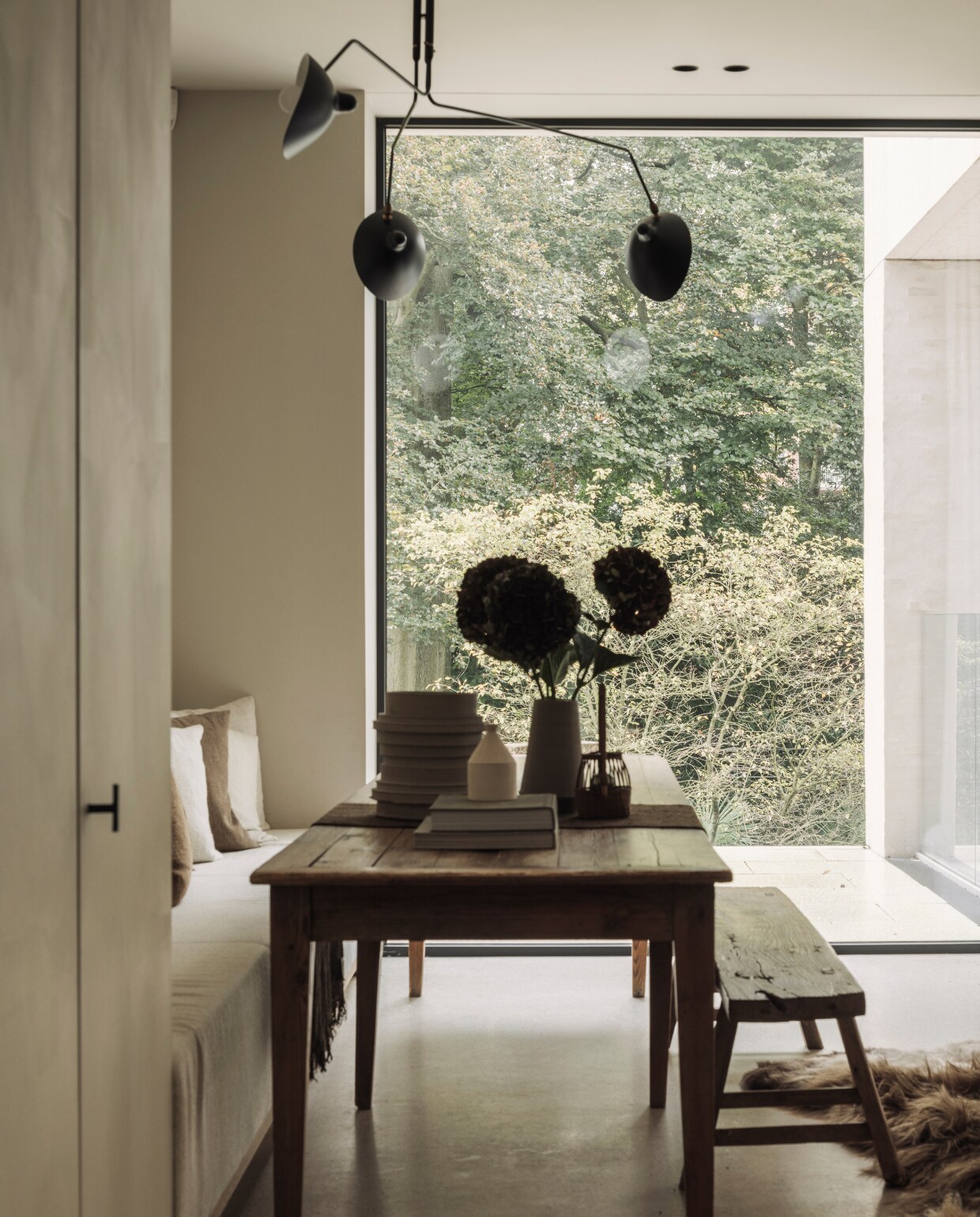 Eettafel van een vlooienmarkt in Barcelona. Lamp van Serge Mouille. De kast en bank eettafel zijn maatwerk. De houten bank komt van The Corner Studio. Vacht van Carine Boxy. stijlvol wonen 01-2025 | fotografie Tijs Vervecken