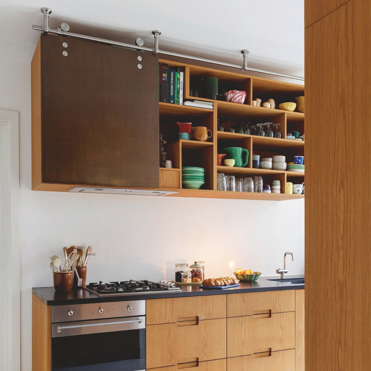 De eikenhouten keuken met werkblad van zwart natuursteen is maatwerk van Studio Flemming Lindholdt. Serviesgoed een mix van de Ursula serie van Royal Copenhagen, schalen van pottenbakker Mette Seedorff, vakantiesouvenirs en erfstukken. vtwonen 12-2024 | styling Rikke Graff Juel | fotografie Christina Kayser