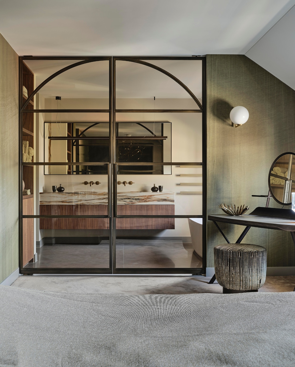 De slaapkamer en badkamer worden gescheiden door dezelfde stalen deuren als in de hal. Kaptafel Cattelan Italia, lamp Flos, poef Bonaldo. stijlvol wonen 08-2024 | Fotografie Space Content Studio