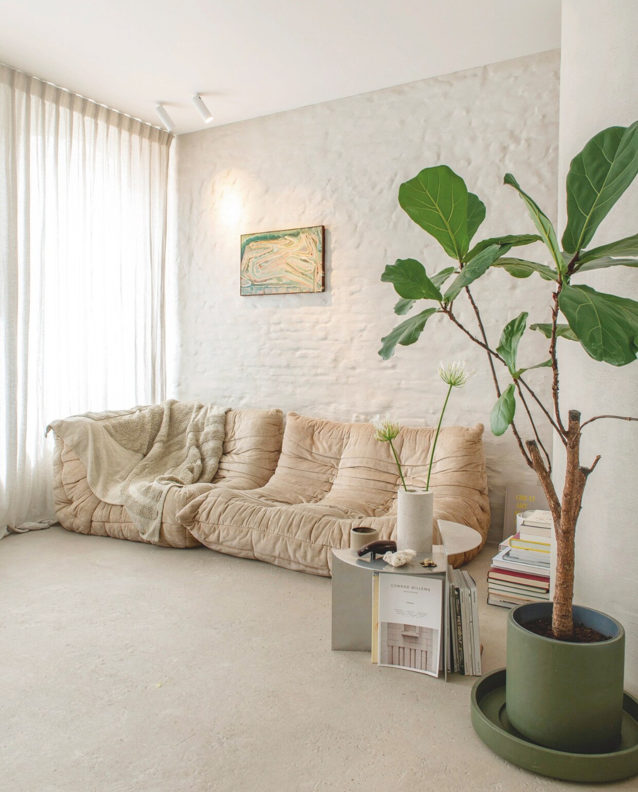 Bank Togo van Ligne Roset, bijzettafel Rivet van Frama, plafondspots Orbit, plantenpot Kaki en schaal Kos eigen ontwerpen voor D&amp;M Deco, vaas SOL van Bultin, kunstwerk van Peter Morrens, linnen gordijnen By Anouk, afwerking wand naturel kalei, afwerking vloer Wabi. vtwonen 13-2024 | styling jeske weel | fotografie caroline coehorst