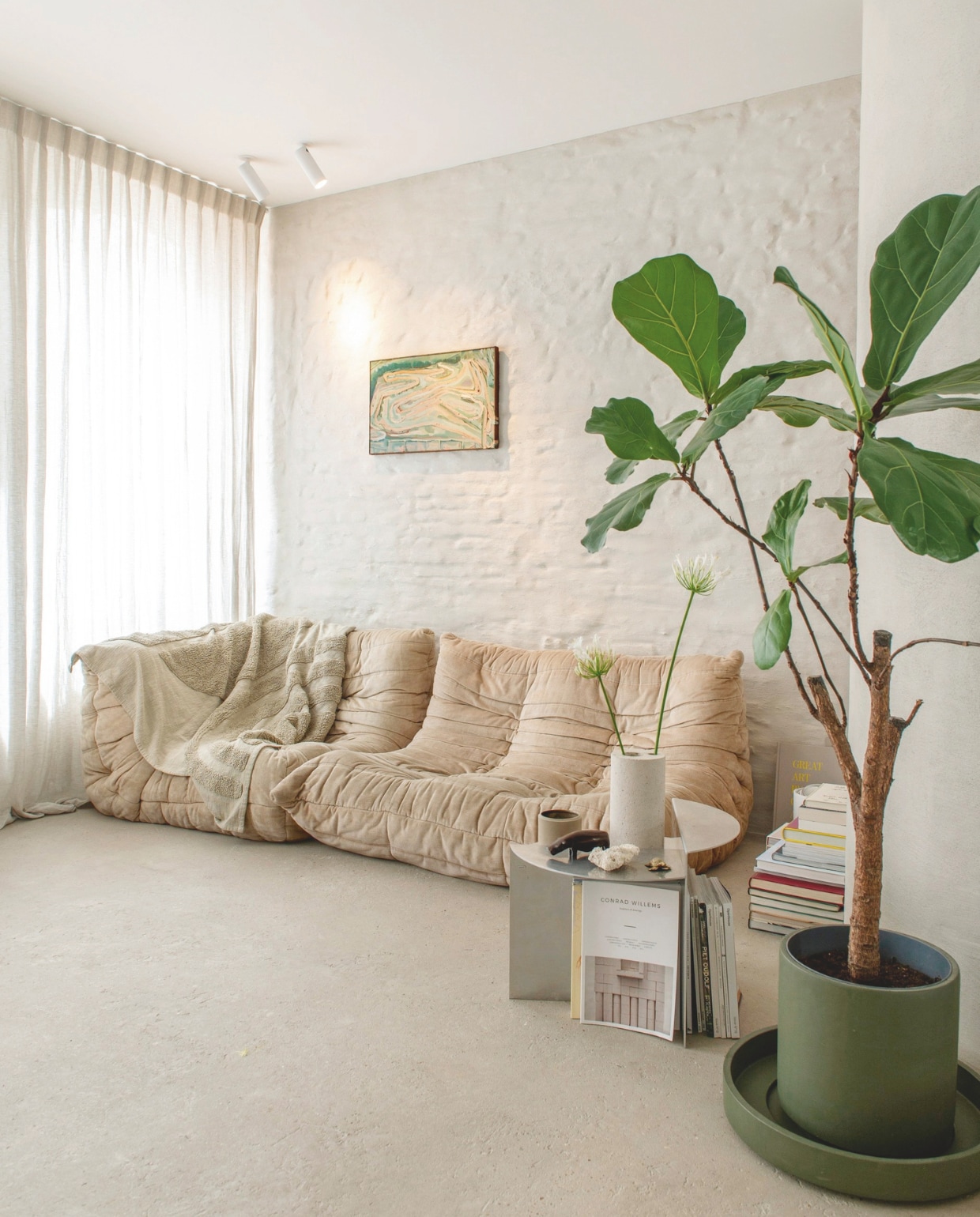 Bank Togo van Ligne Roset, bijzettafel Rivet van Frama, plafondspots Orbit, plantenpot Kaki en schaal Kos eigen ontwerpen voor D&amp;M Deco, vaas SOL van Bultin, kunstwerk van Peter Morrens, linnen gordijnen By Anouk, afwerking wand naturel kalei, afwerking vloer Wabi. vtwonen 13-2024 | styling Jeske Weel | fotografie Caroline Coehorst
