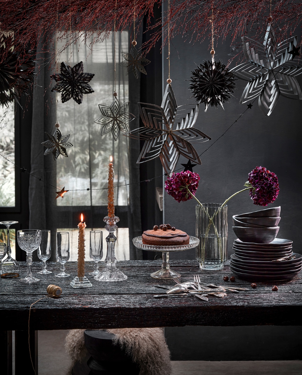Zwart papieren ornament bloem met glitter, 10 cm (Ø) € 5,99, zwarte papieren ster van gerecycled papier, 15,5x3 cm (Øxh) € 2,69, goud- en zilverkleurige slinger met sterren en bolletjes van kunststof, 120 cm (l) € 2,99.M.m.v. karwei.nl (zwart servies, smokey grijze ribbelvaas), vandijkenko.nl (oud zilver bestek). vtwonen 12-2022 | productie Tanja Saarberg, Isa Hoevens | styling Kim van Rossenberg | fotografie Peggy Janssen