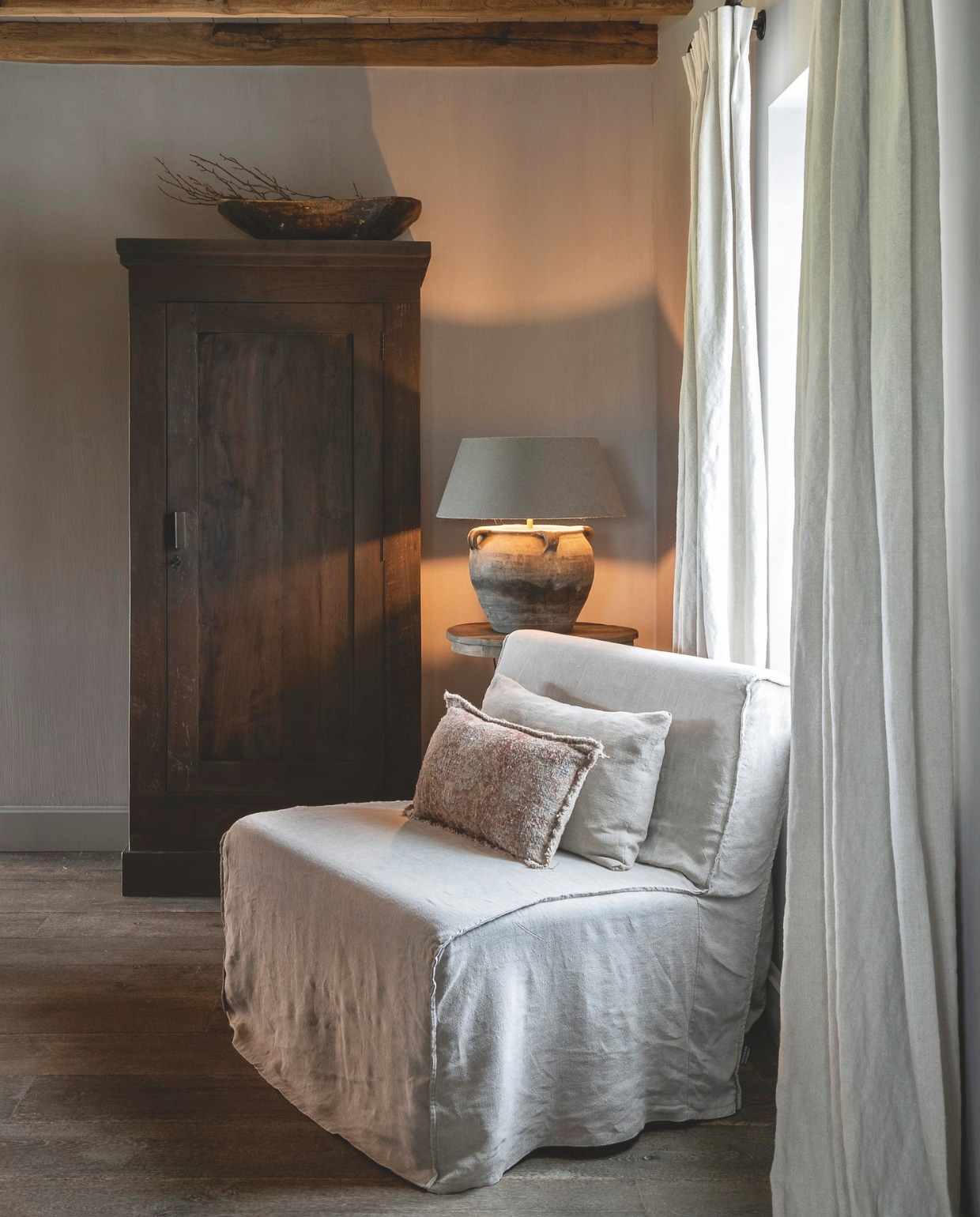 Natuurlijke kleuren en materialen spelen de hoofdrol in de 154 jaar oude woning. Kast Lieke, Chinese terracotta tafellamp en de witte bekleding van de fauteuil van Aura Peeperkorn,kussens van Het Wase Woonhuis. vtwonen landelijk 08-2024 | fotografie Jonah Samyn