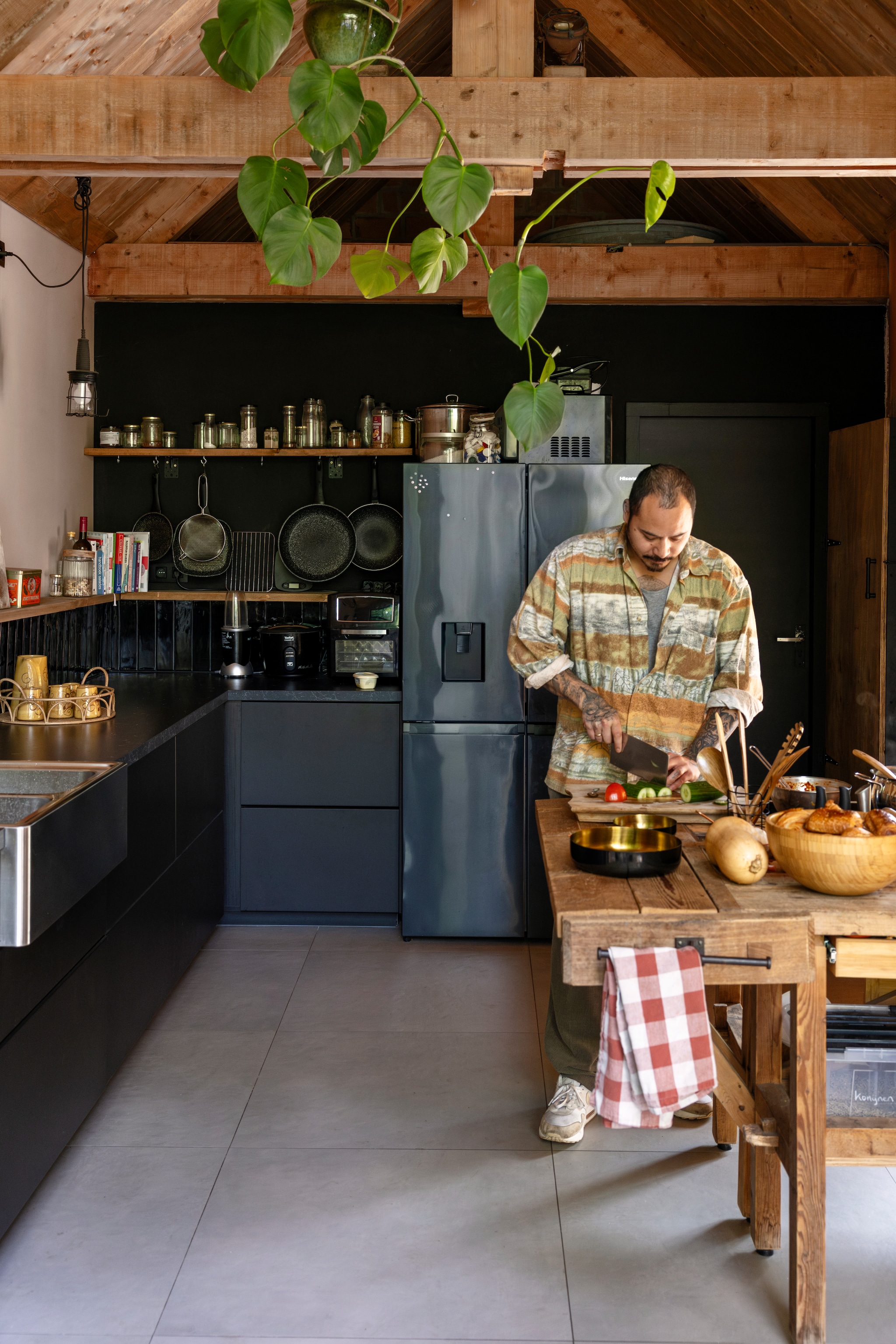 Wandkleur Transcend van Histor, balken gebeitst in Wood Stain Walnut van Spectrum. Betonlook vloertegels 80x80 cm Hornbach. Oude werkbanken ooit gemaakt door de vader en oom van Janneke, kan en mokken Folor, keuken Ikea, koelkast Beko, Air Fryer Mini Oven van Kitchenbrothers, hanglamp Gamma, schalen en handdoek Action. vtwonen 02-2025 | styling Ilona Jongepier | fotografie Dana van Leeuwen | tekst Chris Muyres