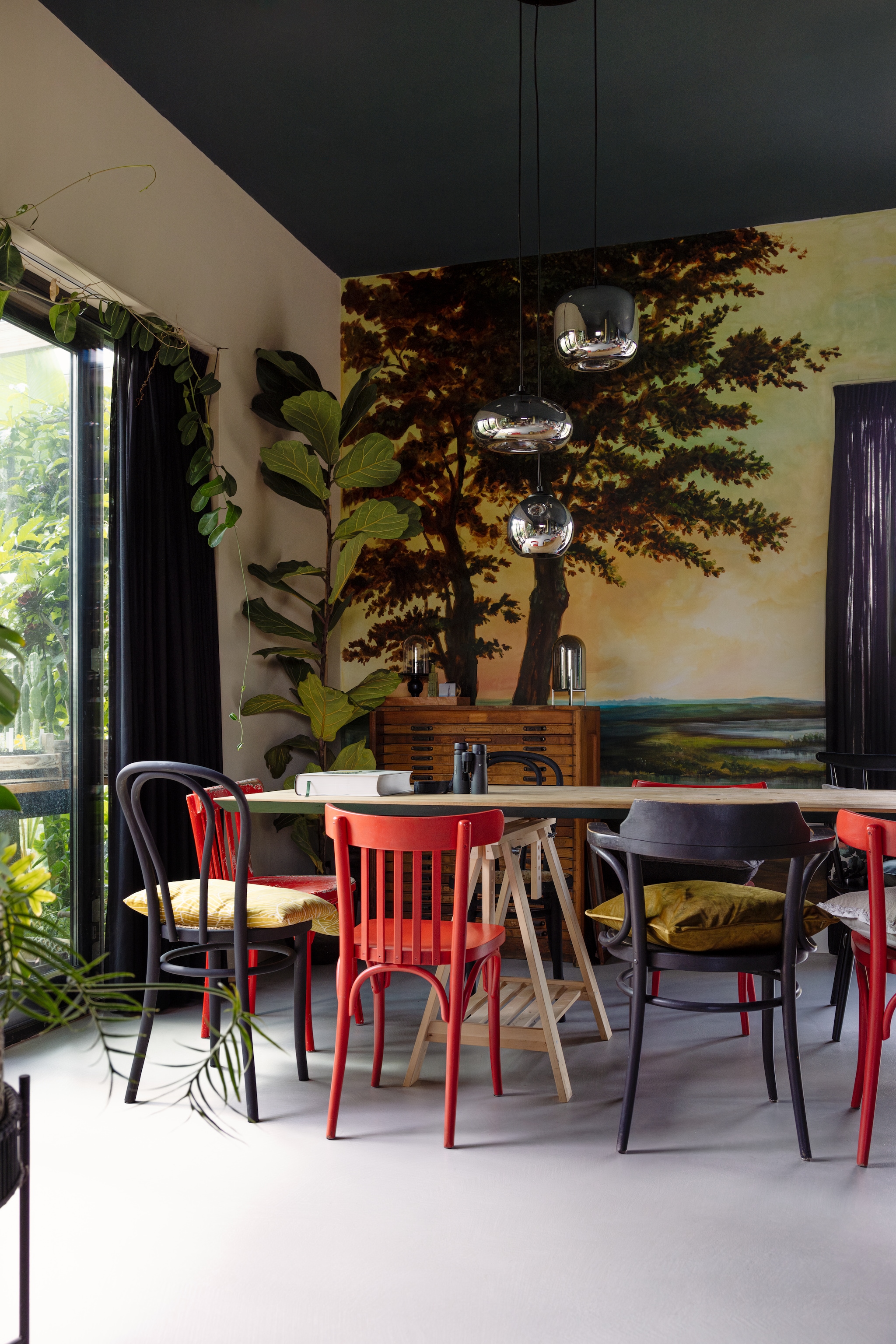 Gietvloer met microtopping M2 Vloeren, muurkleur Aardewerk en plafondkleur Mossel van Gamma, muurschildering door Jessie gemaakt, gordijnen Karwei, eiken tafelblad van R De B Meubels Op Maat, schraag Ikea, vintage stoelen Thonet. Kussens zelfgemaakt en Wehkamp. Plant Ficus Lyrata, tafellamp Present Time. vtwonen 02-2025 | styling ilona jongepier | fotografie dana van leeuwen | tekst Mirjam Rosema-Verhulst