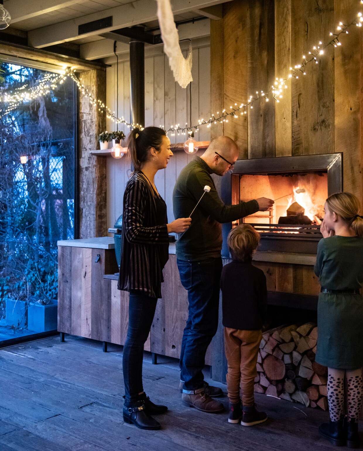 Naast de garage is een buitenkeuken gebouwd, met een constructie van oude meerpalen en stalen ramen. De binnenkant is afgewerkt met barnwood, de haard en houtopslag kregen een stalen lijst. Het werkblad is van beton. Barbecue Green Egg. Lichtjessnoer en lampen van Snoerboer, slinger van Enjoy Ooi. vtwonen 12-2019 | styling Babs Dols | fotografie Louis Lemaire | productie insidehomepage