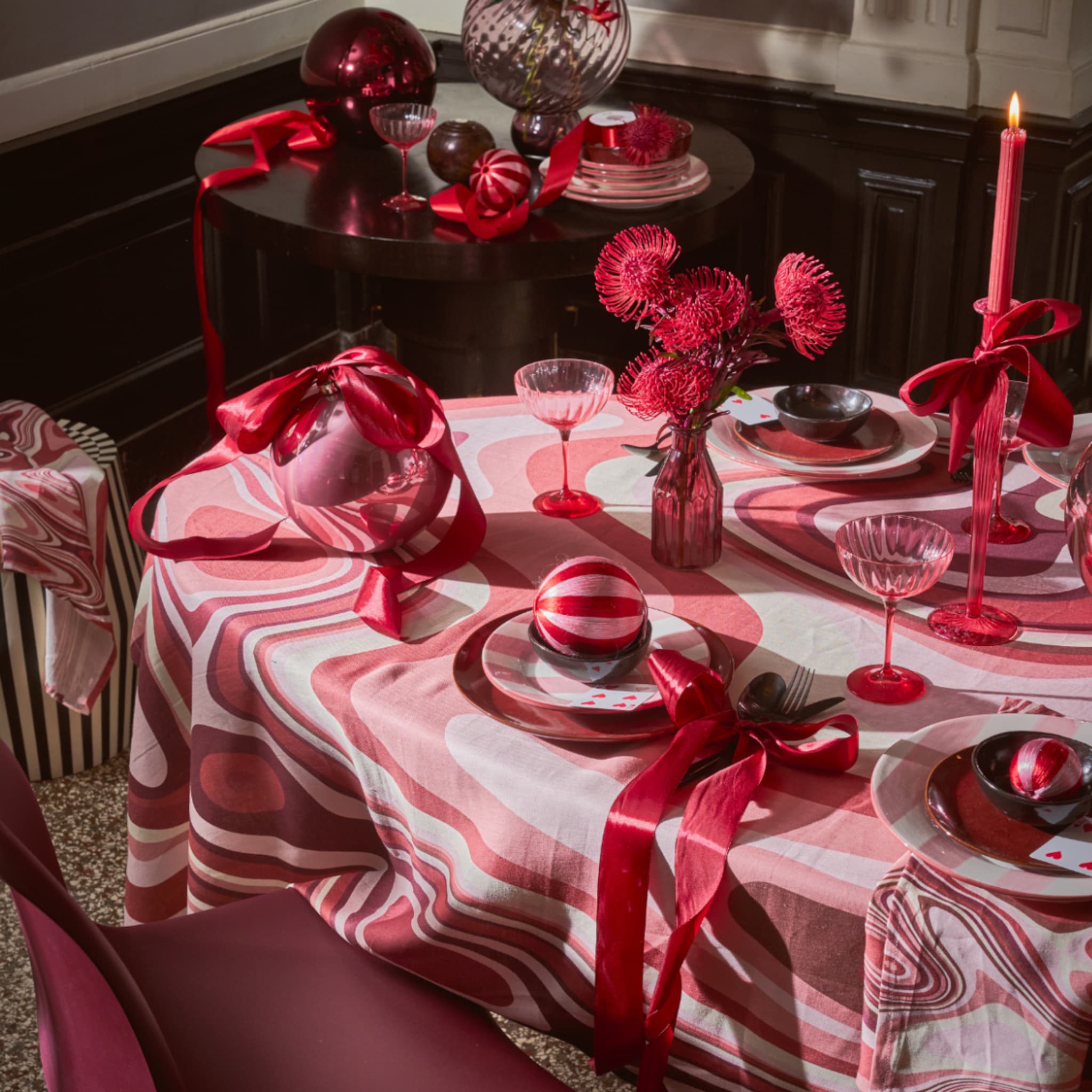 Kersttafel gedekt in roodtinten met rood servies, glas, kaarsen en kerstballen