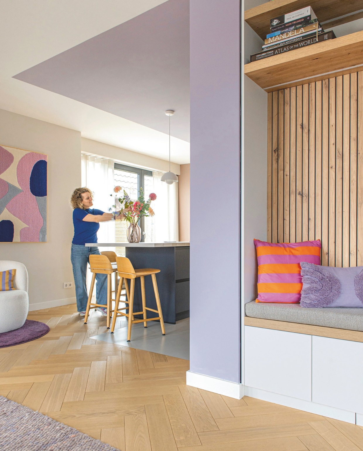Kunstwerk Studio Mirte. Witte fauteuil, kussen Fést. Paars kleed Ikea. Hanglamp Verner Panton, &amp;Tradition. Barkrukken Muuto. Vaas Loods 5. Nis met bank maatwerk van Tritop Interieurbouw. Kussens: lila Blokker, gestreept Xenos. vtwonen binnenkijkspecial 11-2024 | styling jeske weel | fotografie caroline coehorst