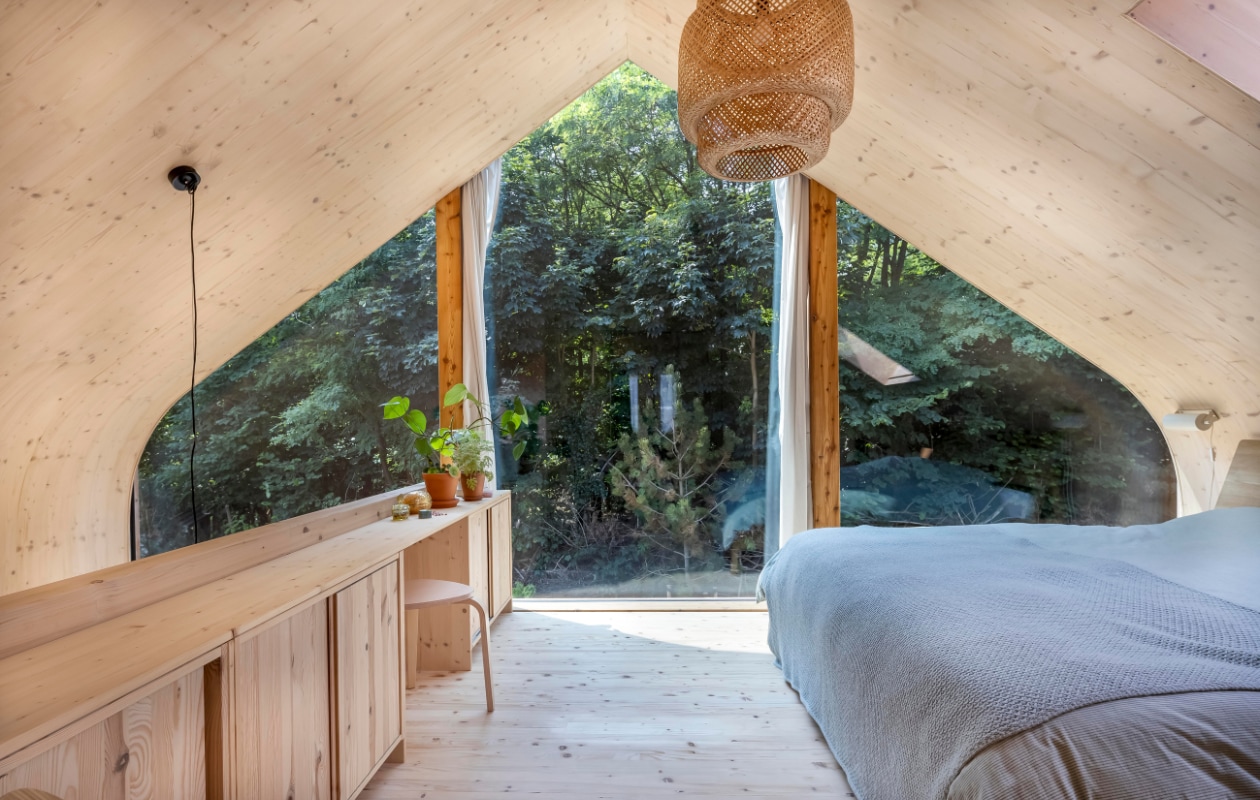 Ook de balustrade in de slaapkamer heeft kastruimte en een zitplek. Door de glasgevel komt het bos binnen. Hanglamp, groen beddengoed Ikea. Sprei Sissy-Boy, eiken bed Ethnicraft. vtwonen 01-2025 | fotografie Hennie van Belkom | tekst Christine van der Hoff