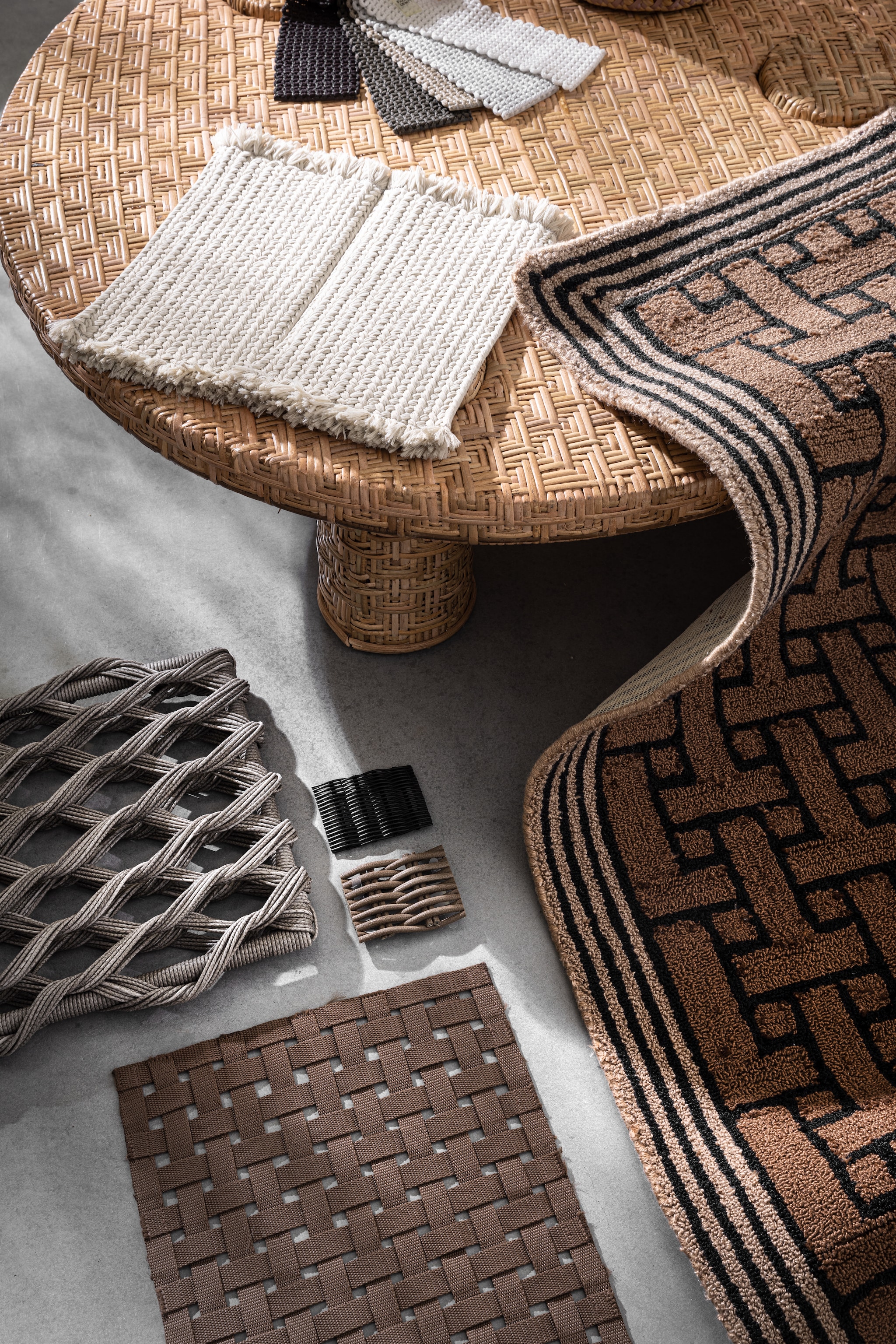 Vloerkleed T Monogram outdoor van Ted Bakerin Light Brown, gerecycled pet, 140x200 cm € 299,-(vloerkledenwinkel.nl). Rotan salontafel, 101x32,5 (Øxh) € 595,- (hkliving.com). Tapijtstaal met kwastjes Sahara van Paola Lenti in S01, polyolefin, acrylvezel en polyurethaan, gevlochten stofstalen Aero van Paola Lenti, grote gevlochten stalen in grijs en bruin en kleine gevlochten stalen van Paola Lenti in zwart en bruin (dacks.nl). styling marlies does | fotografie peggy janssen
