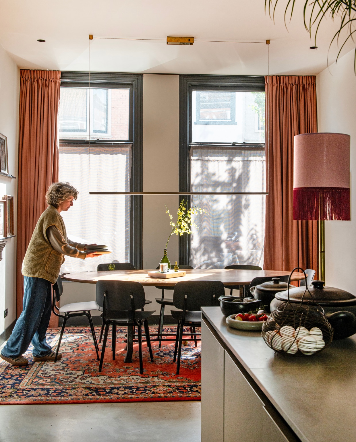 Schemerlamp Madame Garage, eiermand kringloop, zwarte potten en pannen uit Brazilië, hanglamp Piet Hein Eek, tafel uit kringloopwinkel voorzien van gerecyclede fineerlaag door Combitex, stoelen Revolt van Friso Kramer heruitgebracht door Hay, Perzisch tapijt Rozenkelim, gordijnen Karwei. vtwonen 01-2025 | productie De Binnenkijkers | fotografie Caroline Coehorst