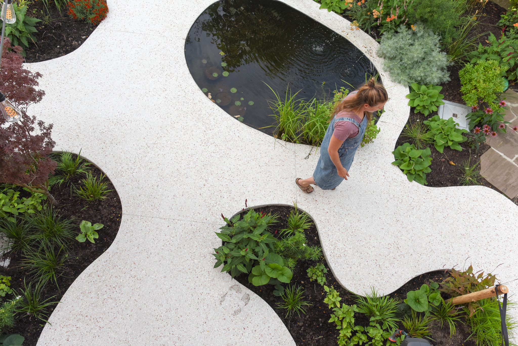 Vijverplanten: watermunt, gele lis en waterlelie. Het tuinpad is van terrazzobeton - beton gemengd met stukjes marmer, zandsteen, graniet of glas. vtwonen TUIN 01-2025 | fotografie Veronique De Walsche
