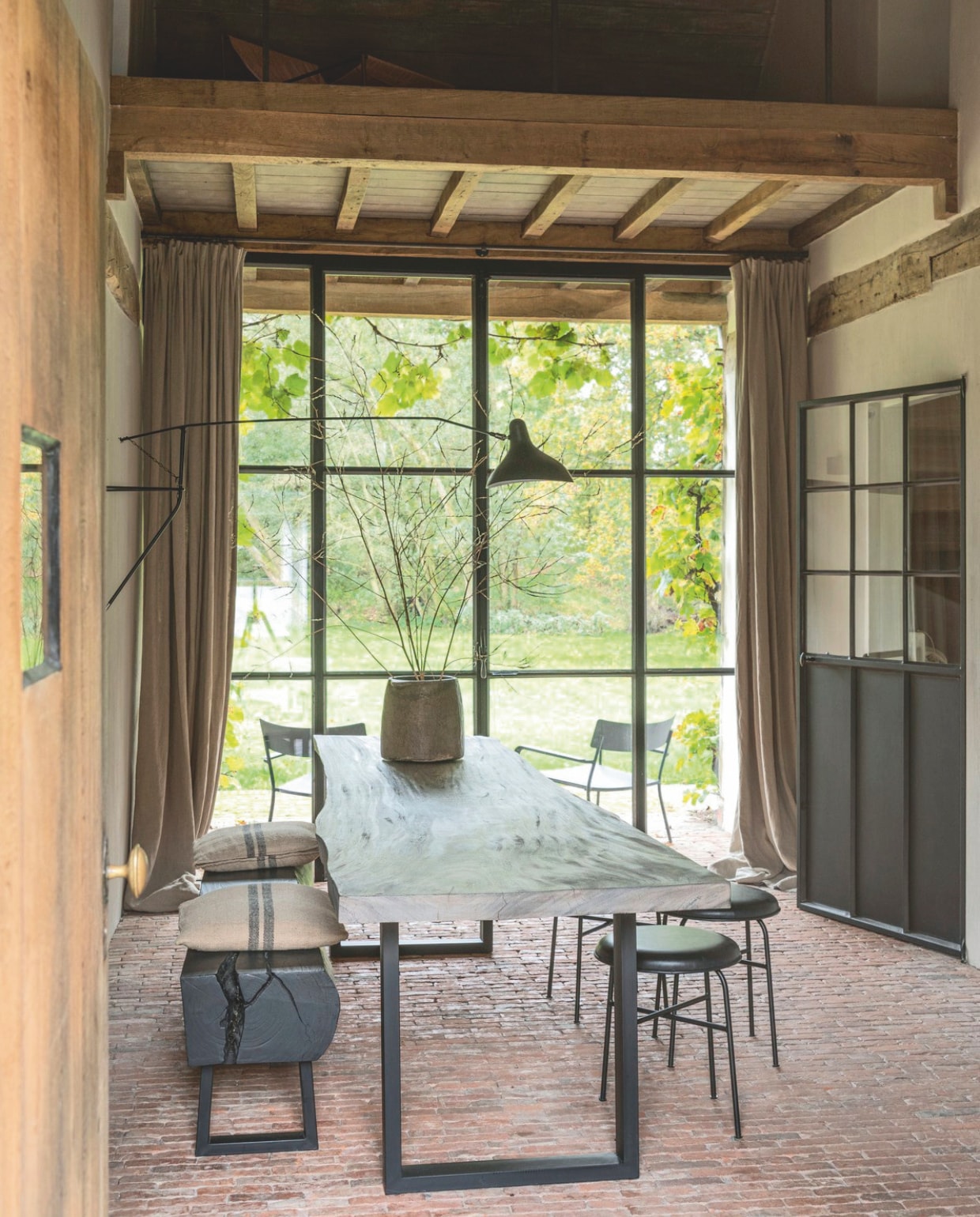 Bakstenen vloer originele vloer van de boerderij. Houten tafel en bank Moka Tales. Krukken Menu. Tuinstoelen van Vincent Van Duysen voor Serax. Metalen kast vintage. Lamp Serge Mouille. vtwonen landelijk 01-2025 | styling Marc Heldens | fotografie Verne Photography