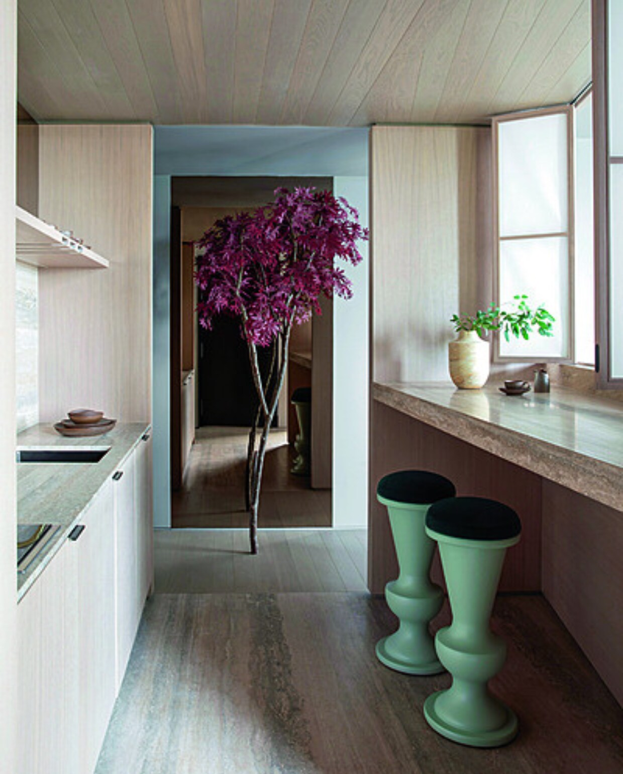 Houten maatwerk kasten en de travertin vloer en tafelblad blenden tot een natuurlijk en licht geheel. Ook hier voegt een rode esdoorn een Japanse toets toe aan het interieur. Stijlvol Wonen 01-2025 | productie Living Inside | fotografie Ruth Maria Murphy