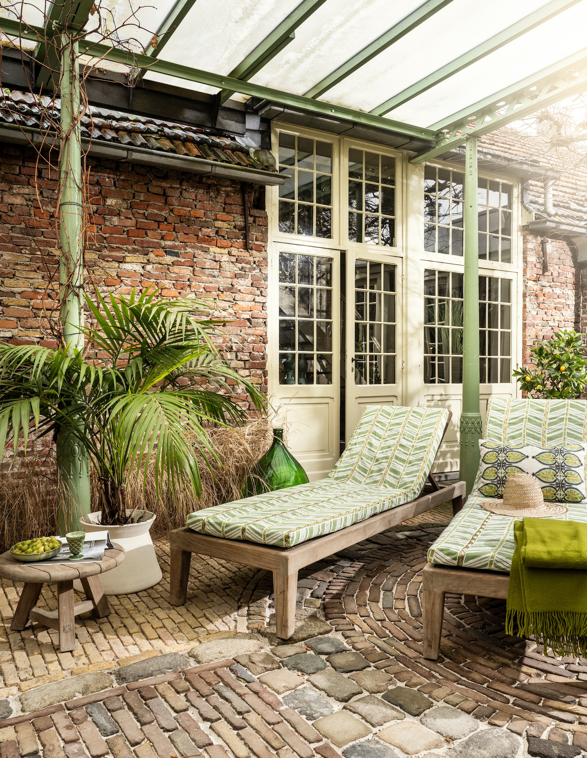 Hardstenen kasseien, per m² € 102,85, glazen fles € 120,-, teakhouten buitentafel Anton van Gommaire, set van 3 € 2165,-, outdoor loungebed Lisa van Gommaire, teakhout en PE-vlechtwerk, 209x66x35 cm (lxbxh) € 1774,- (achterhuis.nl). Matrashoes van stof Woodbridge Stripe van Nina Campbell in NCF4504-05, linnen met borduursels, per meter € 169,-, kussen van William Yeoward € 125,- (wva.nl). Lamswollen plaid Boston 444 € 131,95 (aabe.nl). Terracotta bloempot Kulma Sand van Urban Nature Culture, 45x32 cm (Øxh) € 169,- (shop.vtwonen.nl). Porseleinen beker € 69,- (ottomania.nl). Porseleinen diep bord Chef Ceramics € 15,95 (hkliving.com). Strohoed prijs op aanvraag (bydennis.nl). Overig privébezit.