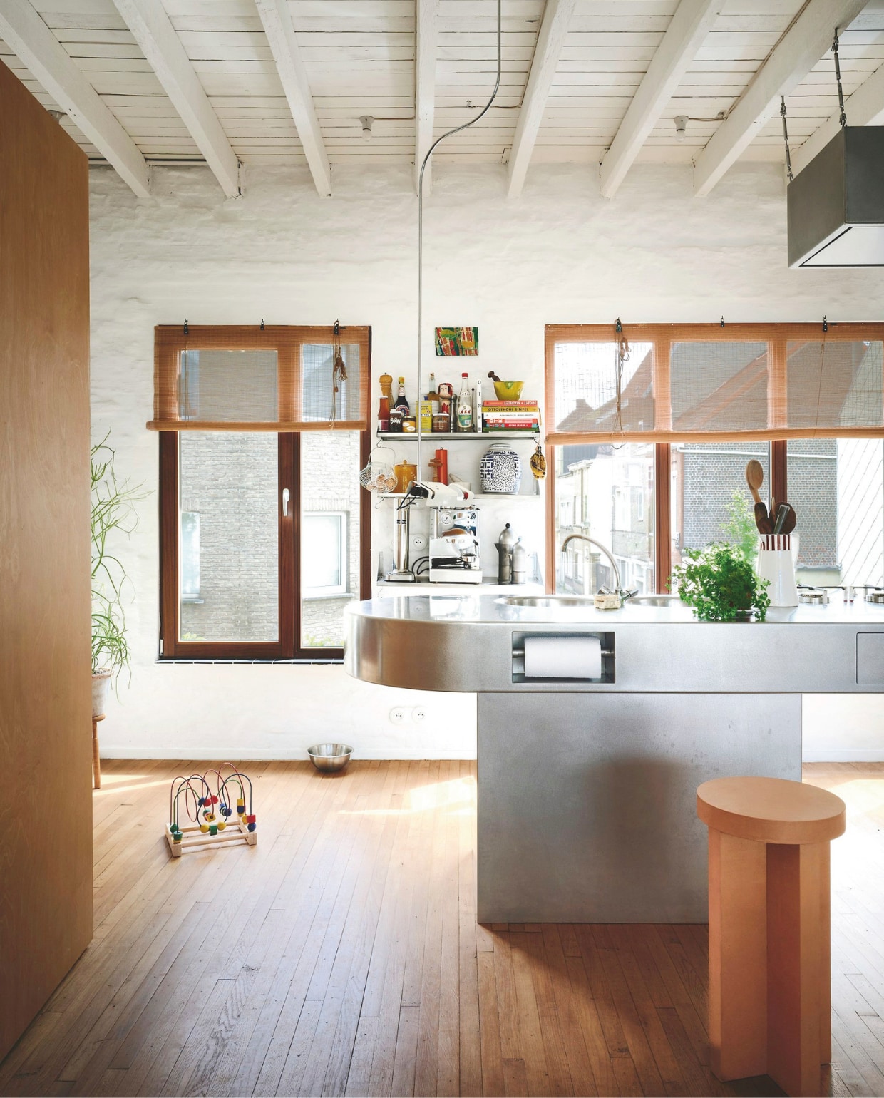 De keuken aan de voorzijde van het huis bevat een pronkstuk: het op maat gemaakte keukeneiland in rvs en staal, een eigen ontwerp in samenwerking met Bossuyt Kitchens. Opvallend: de details, zoals de keukenrolhouder, die verwerkt zijn in het keukeneiland. Op de wandplank staat onder andere koffiepot een La Cupola van Alessi en een carbonator van Aarke. Kunstwerk van Rosa Roberts. stijlvol wonen 02-2025 | productie Living Inside | fotografie Mr. Frank