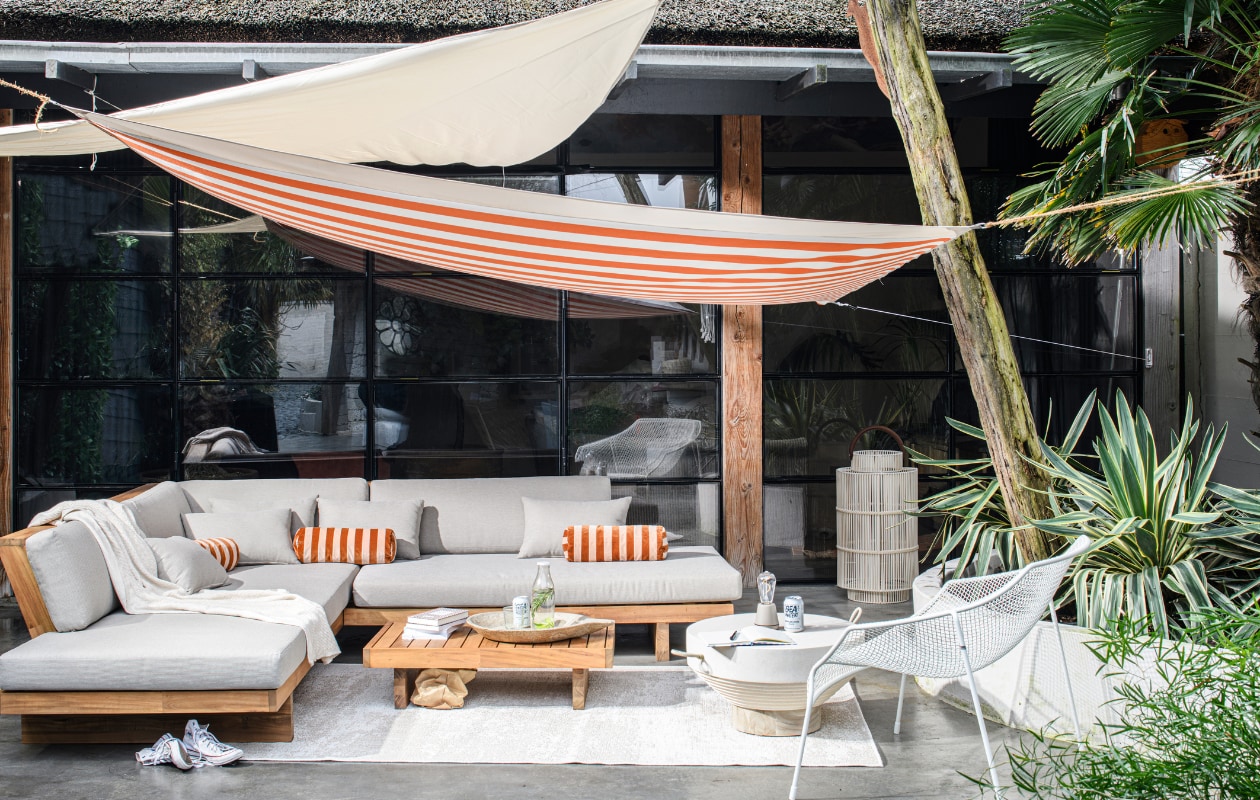 Acaciahouten loungeset van Nous Garden, 269x269x70 cm (bxdxh), binnen- en buitenkleed van Nous Living, gerecycled pet, 230x160 cm (wehkamp.nl). Plaid Pergamon in wafelstructuur, katoen en wol, 130x170 cm, outdoor salontafel Jimbaran, glasvezel en teakhout, 80 cm (Ø), outdoor lantaarn Bartolome XL, kunststof, glas, metaal (rivieramaison.com). Gestreepte katoenvelours rolkussenhoes Bolster (christinalundsteen.com). Marmeren schaal (rawmaterials.eu). Gepoedercoat stalen loungestoel Heaven (emu.it). Notitieboek (flyingtiger.nl). Glazen fles, glas, gerecycled glas (dille-kamille.nl). Oranje-wit gestreepte outdoor stof Dralon, waterafstotend acryl met teflonlaag, stofbreedte 160 cm, per meter (stoffamstueck.de). Schaduwdoek Hold-An, uv-beschermd polyester, 300x300 cm, driehoekig schaduwdoek Hold-An, 300x300 cm (jysk.nl). vtwonen tuin special 10 | styling Marit Saladini | fotografie Louis Lemaire | assistentie Rosa van Schie en Kiki de Koning